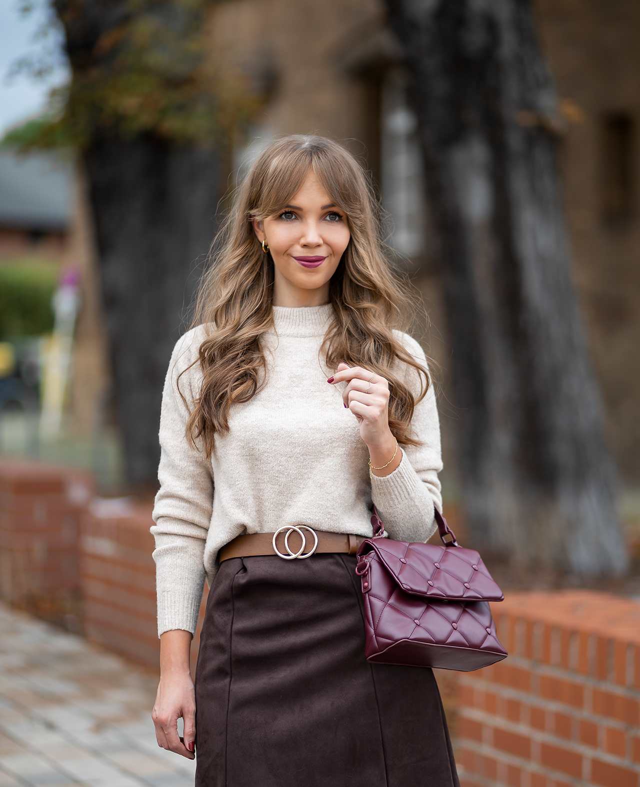 Frau in weißem Strickpullover, kombiniert mit dunkelbraunem Rock und lila Handtasche als Wiesn Outfit