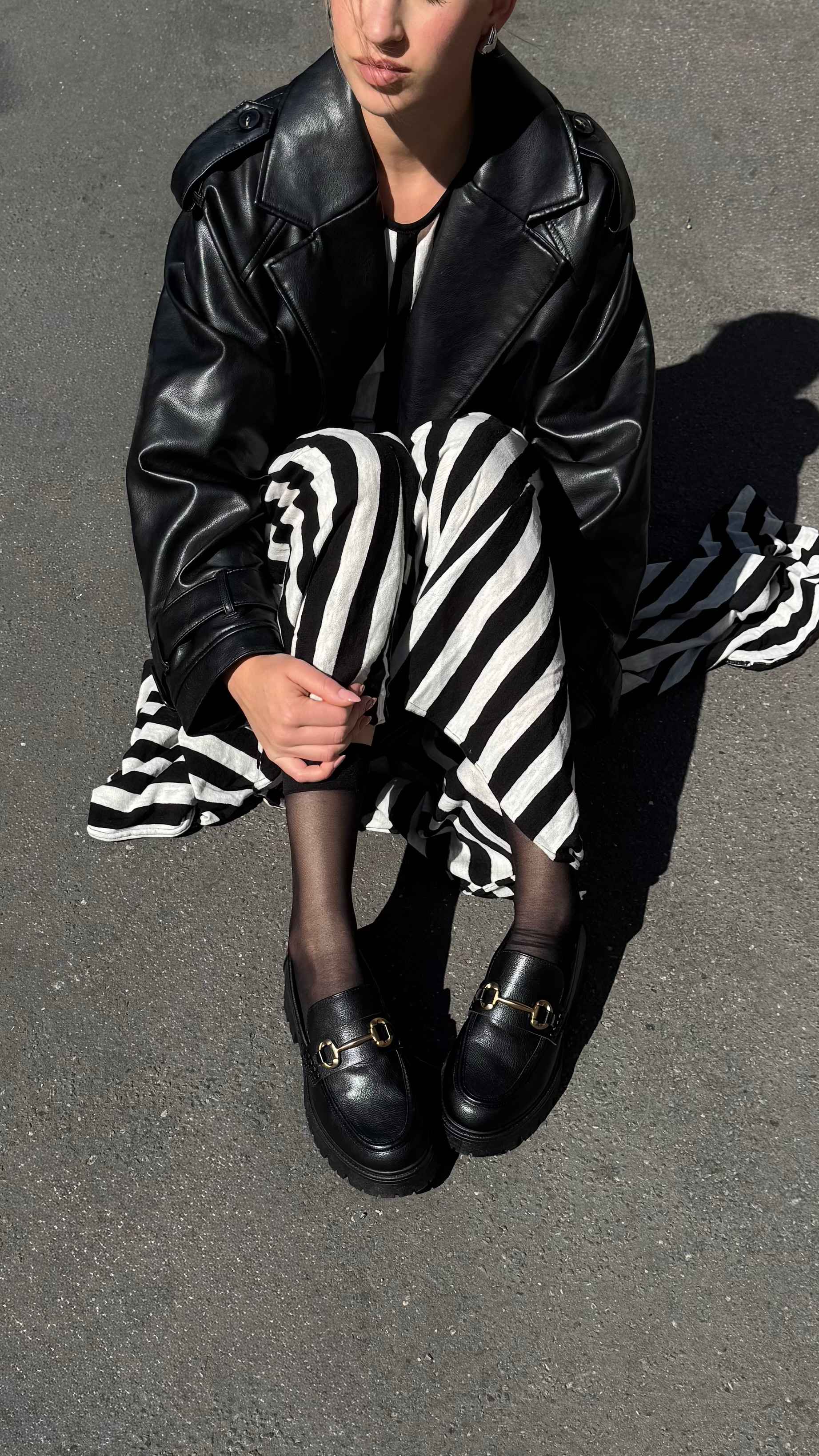 Frau in Zebrastreifen-Kleid und schwarzer Lederjacke sitzt auf Asphalt