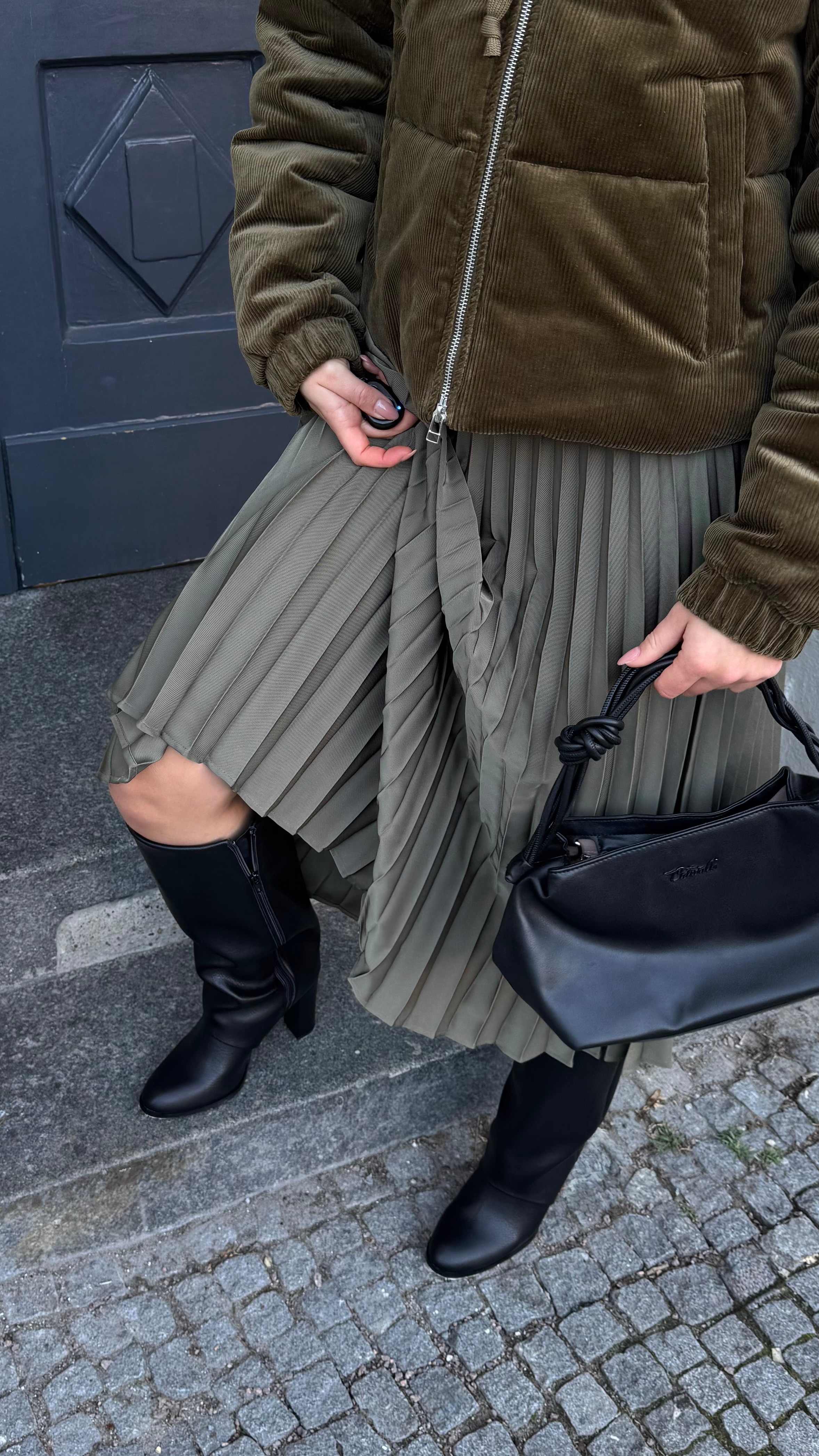 Frau in salbeifarbenem Rock und schwarzen Underknee Boots, stehend auf einer Treppe