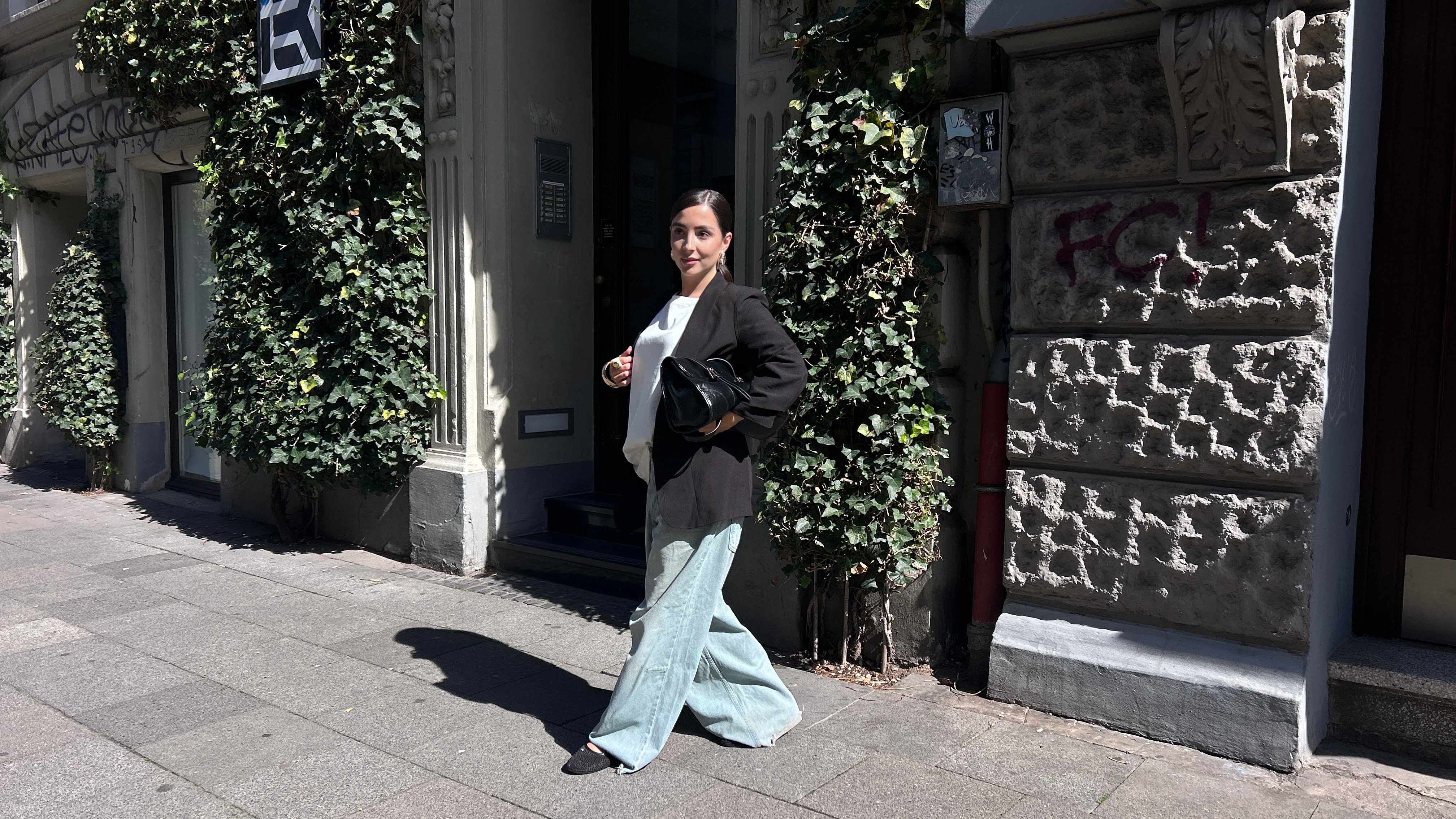 Frau in schwarzem Blazer, kombiniert mit Wide Leg Jeans vor efeubewachsener Mauer