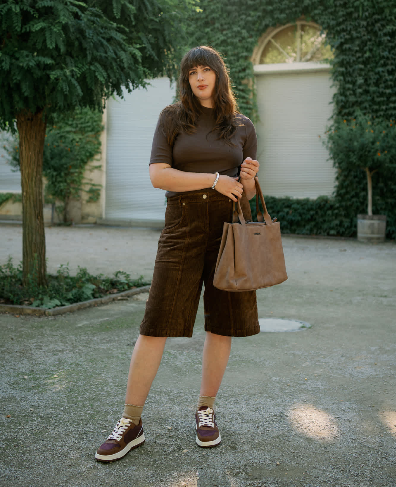 Frau in braunem All-Over-Outfit, mit Top, Cargoshorts, SNeakern und passender Bag