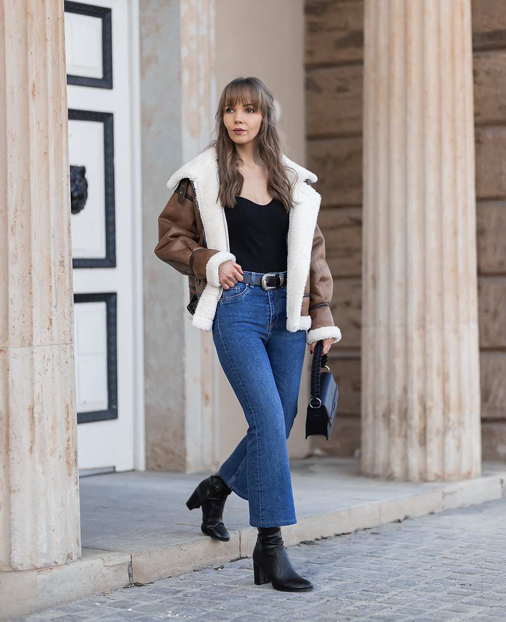 Frau in Skandi-Chic mit blauer Jeanshose, schwarzem Top und braunem Fellmantel auf Treppe