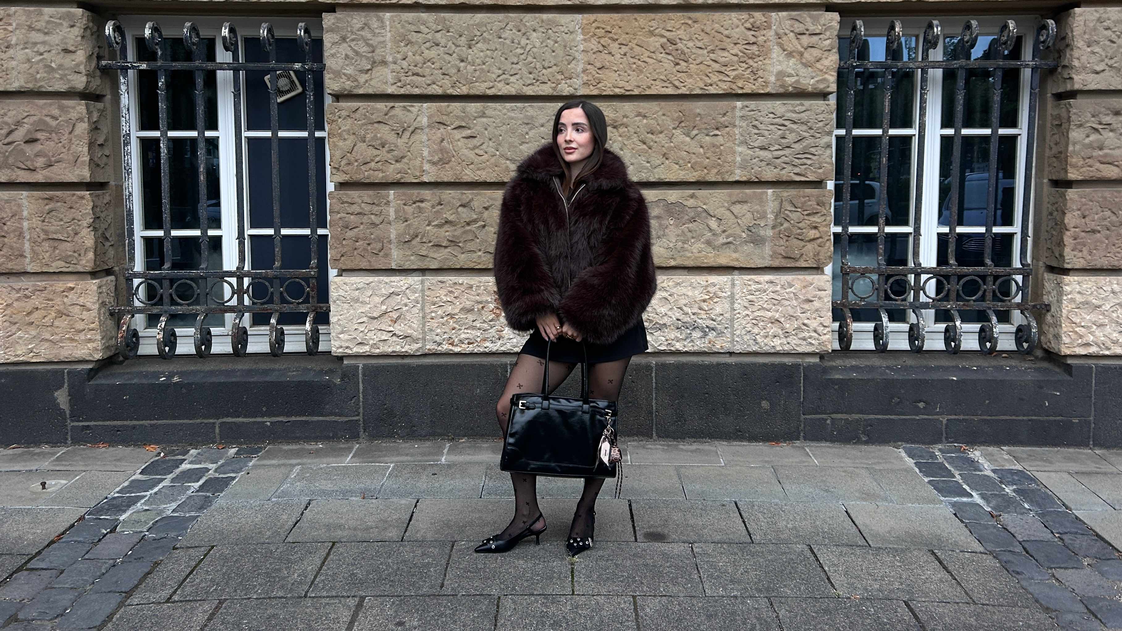 Frau in Kunstfellmantel, hält Handtasche, trägt Strumpfhose zum Outfit