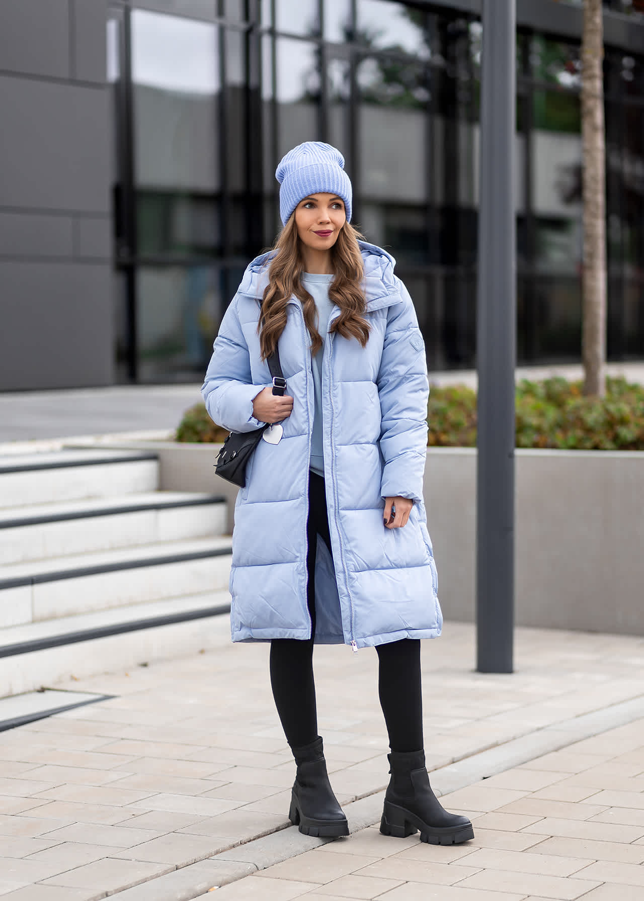 Frau in eisblauem Wintermantel mit passender Mütze und Handtasche