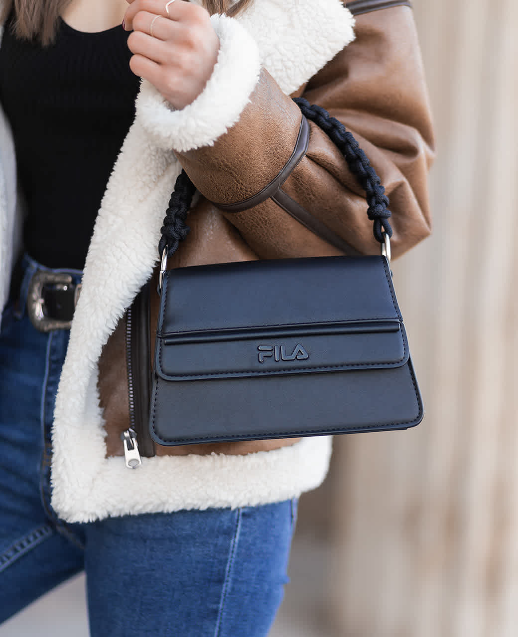 Frau mit brauner Fell-Jacke trägt schwarze FILA-Handtasche am Arm