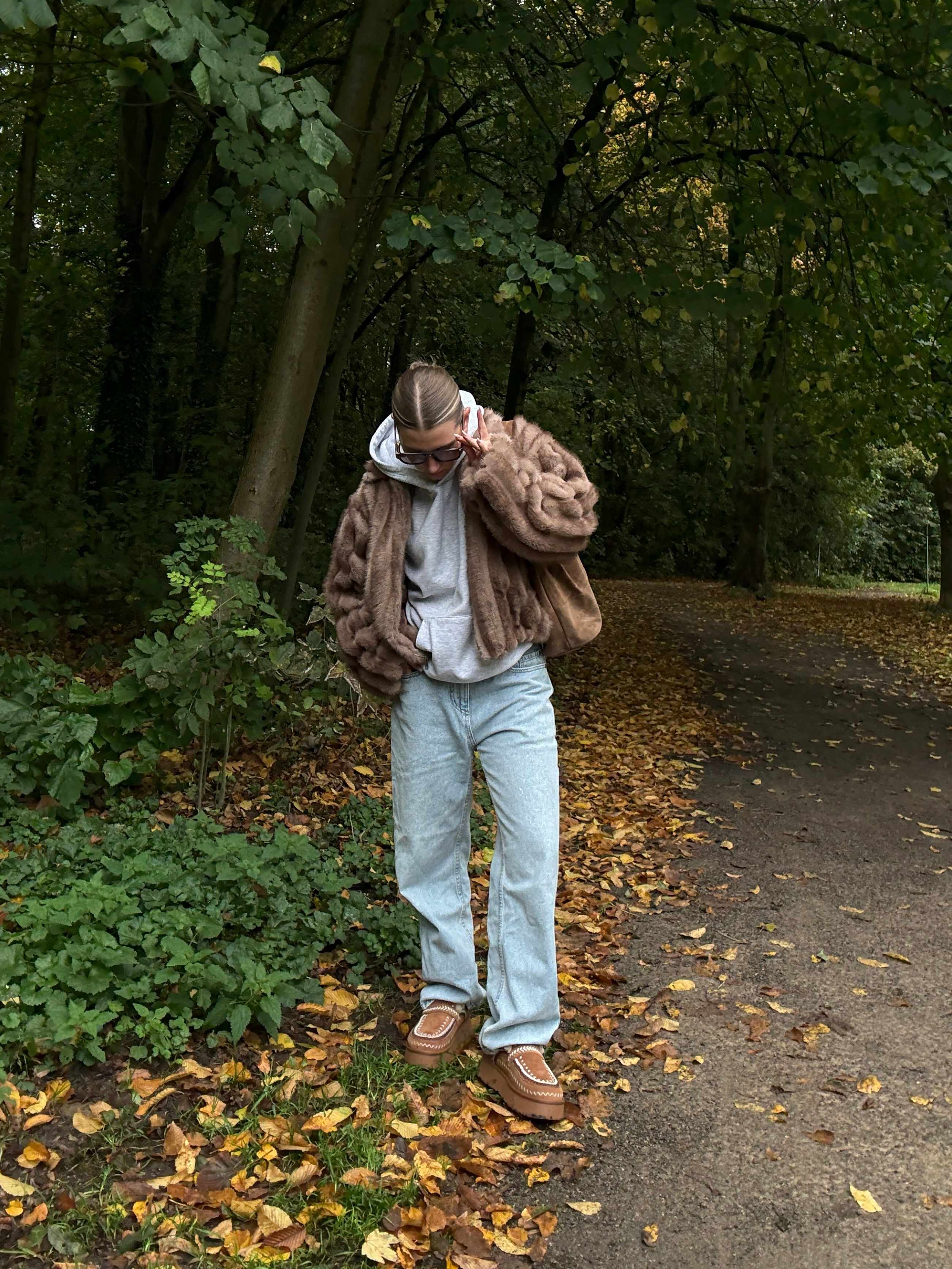 Frau steht an Parkweg, trägt kuscheliges Outfit mit Slippern, Jogginghose und flauschigem Sweater