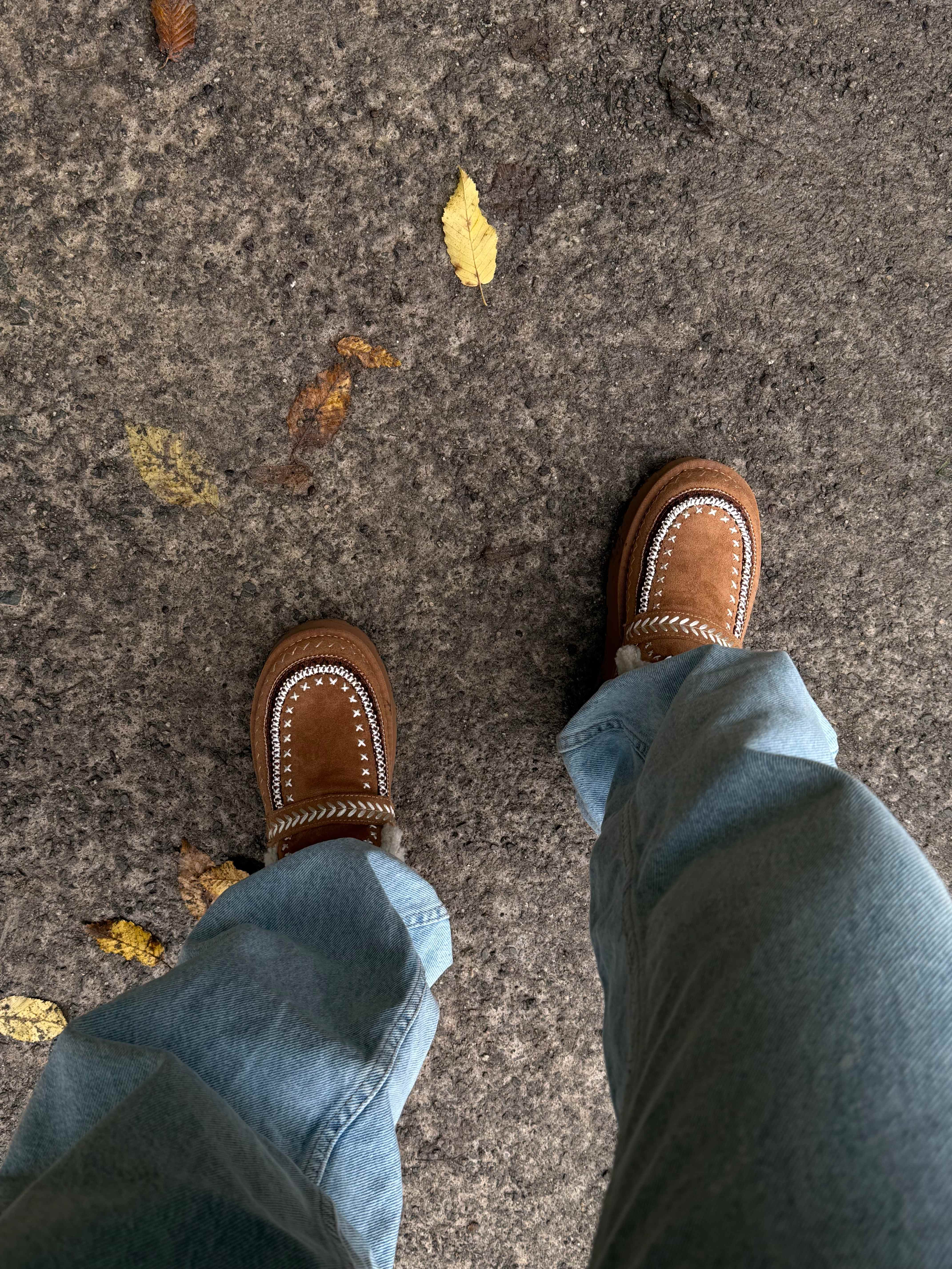 Top-Down Ansicht einer Person mit braunen Slippern, stehend auf Parkweg
