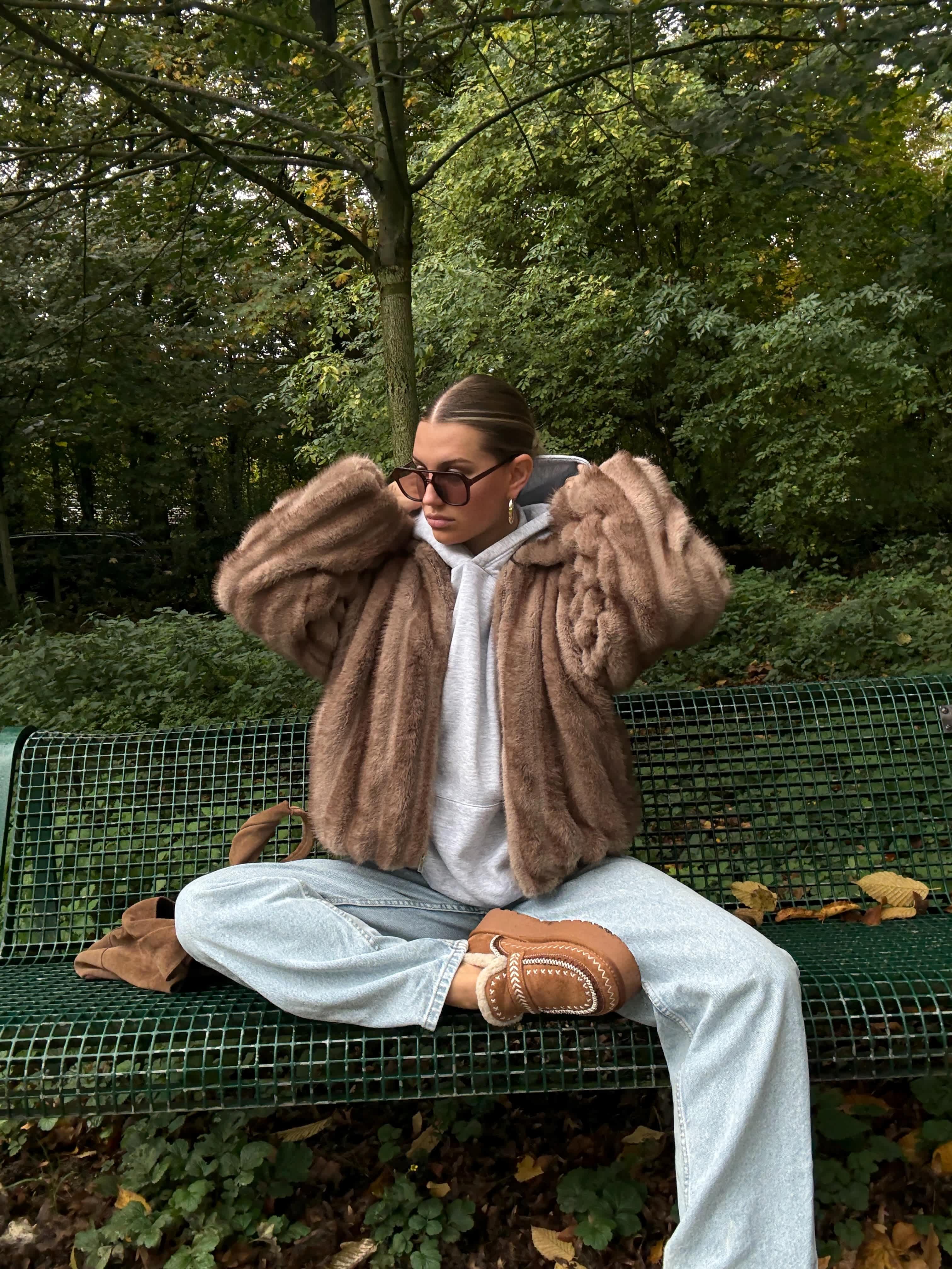 Frau sitzt in Park, auf grüner Parkbank, trägt flauschiges Outfit