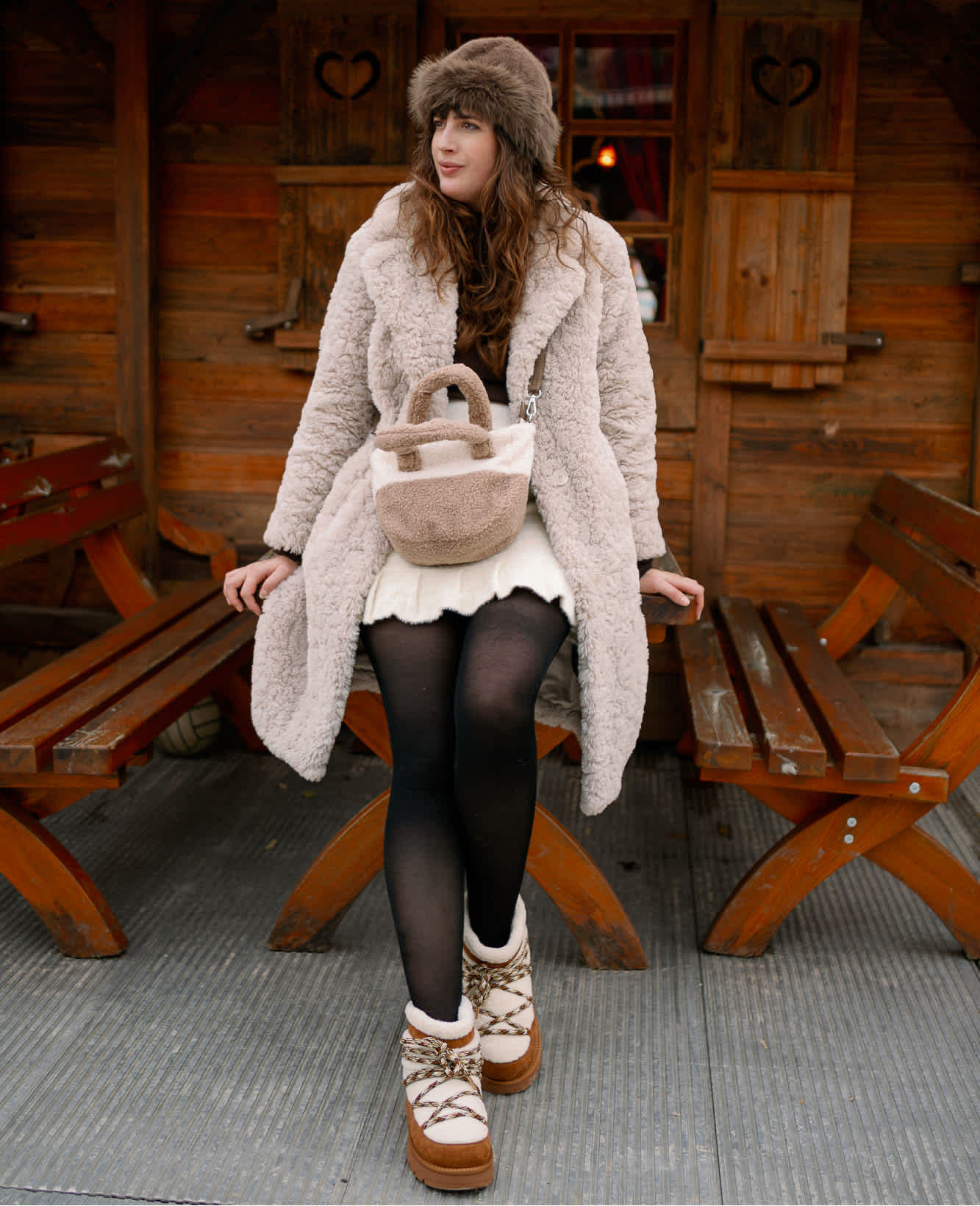 Frau in kuscheligem Winter-Outfit mit Cozy Boots, lehnt an braunem Holztisch