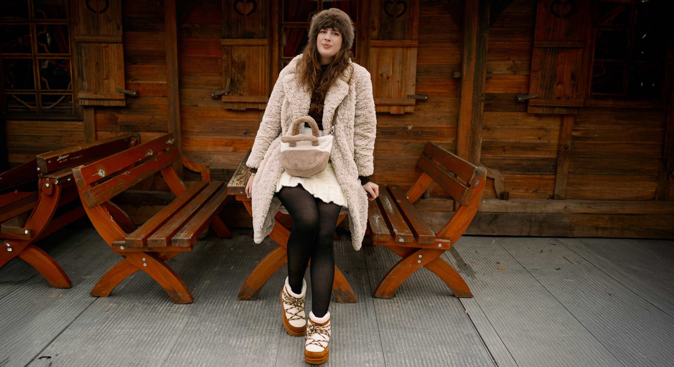 Frau in winterwarmem Outfit mit Cozy Boots lehnt an Holztisch