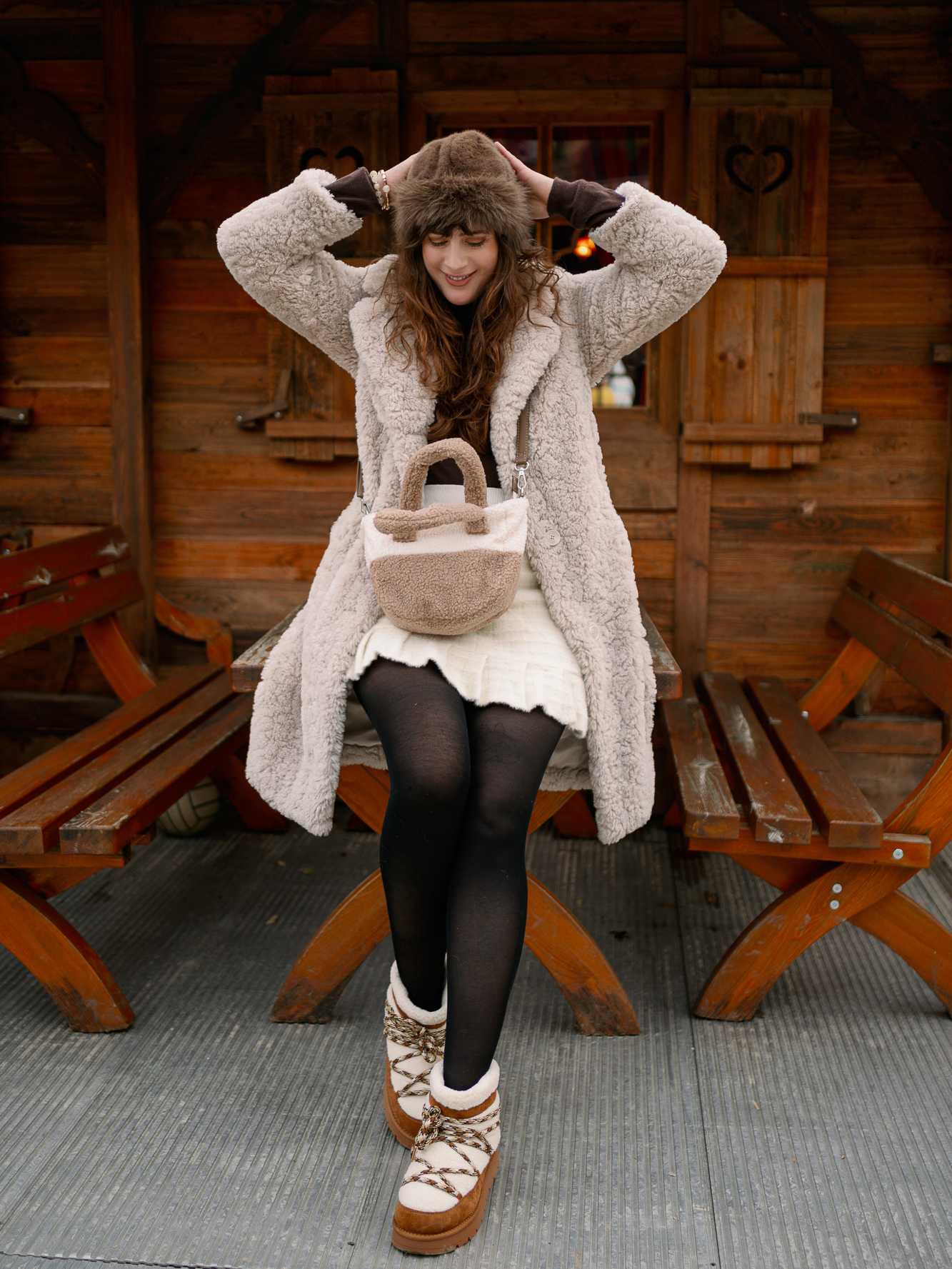 Frau in flauschiger Jacke und Cozy Boots sitzt lächelnd auf Holzbank