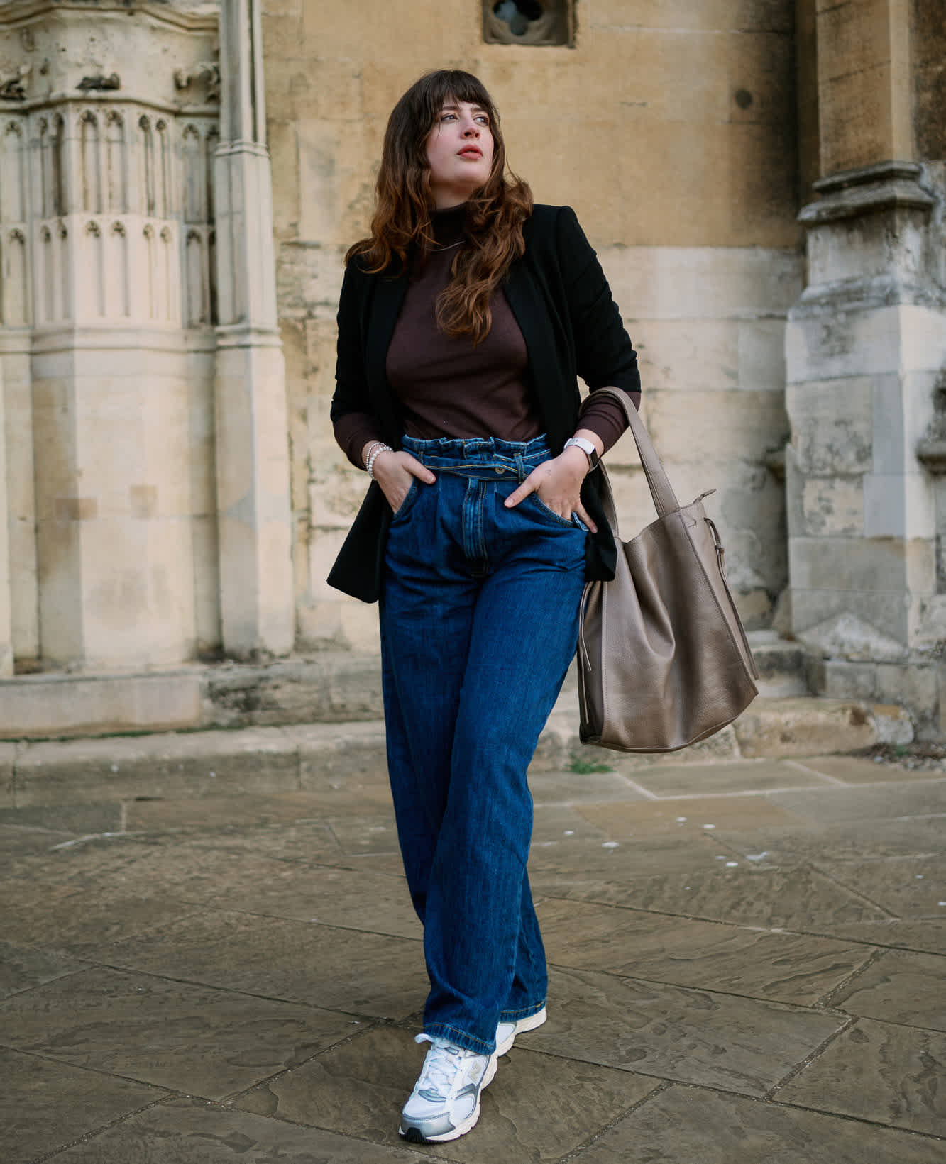 Frau in Normcore-Outfit, trägt schwarzen Pullover mit blauer Jeanshose und Sneaker-Schuhen