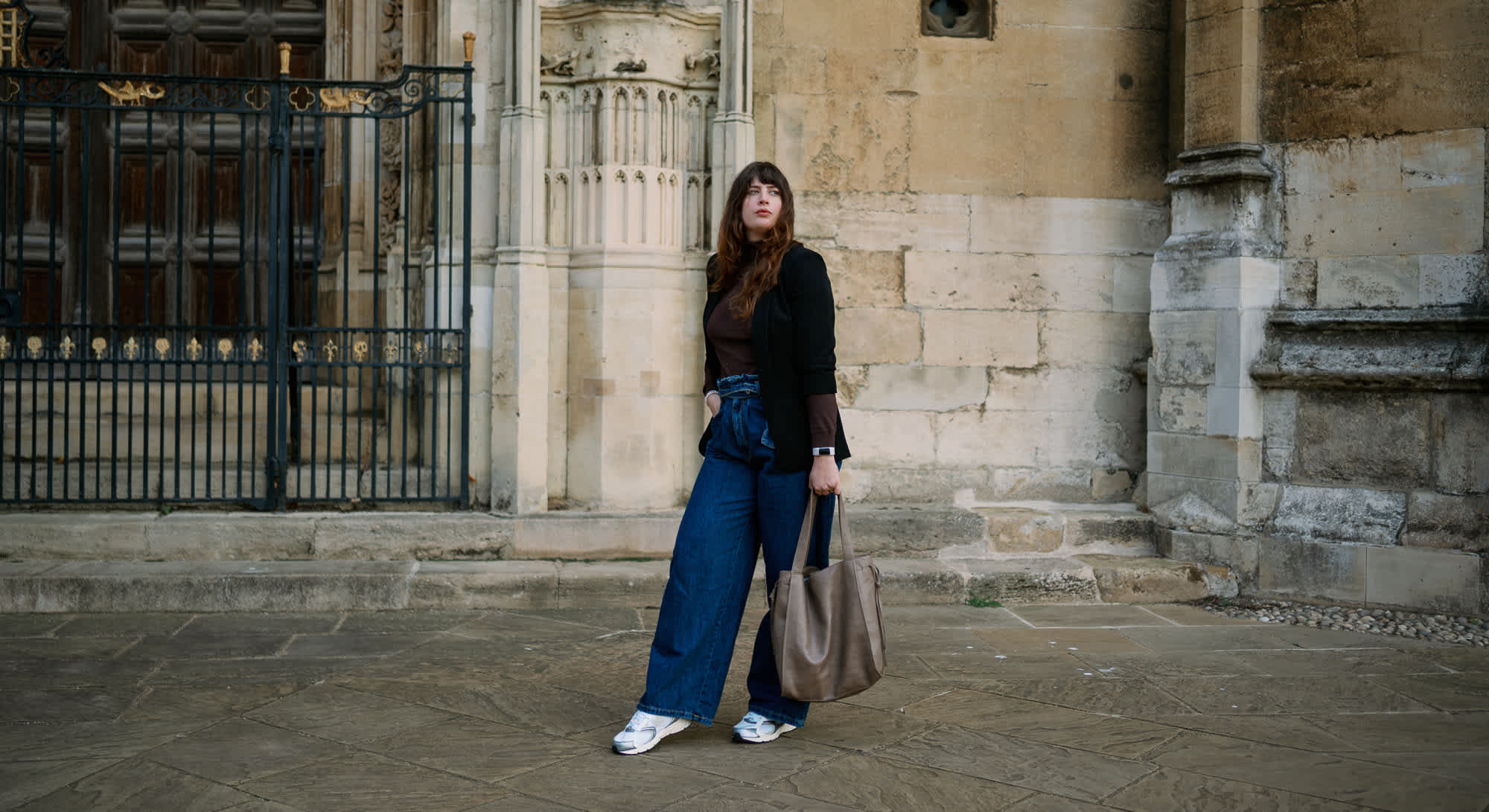 Frau in Normcore-Outfit posiert vor Steinfassade