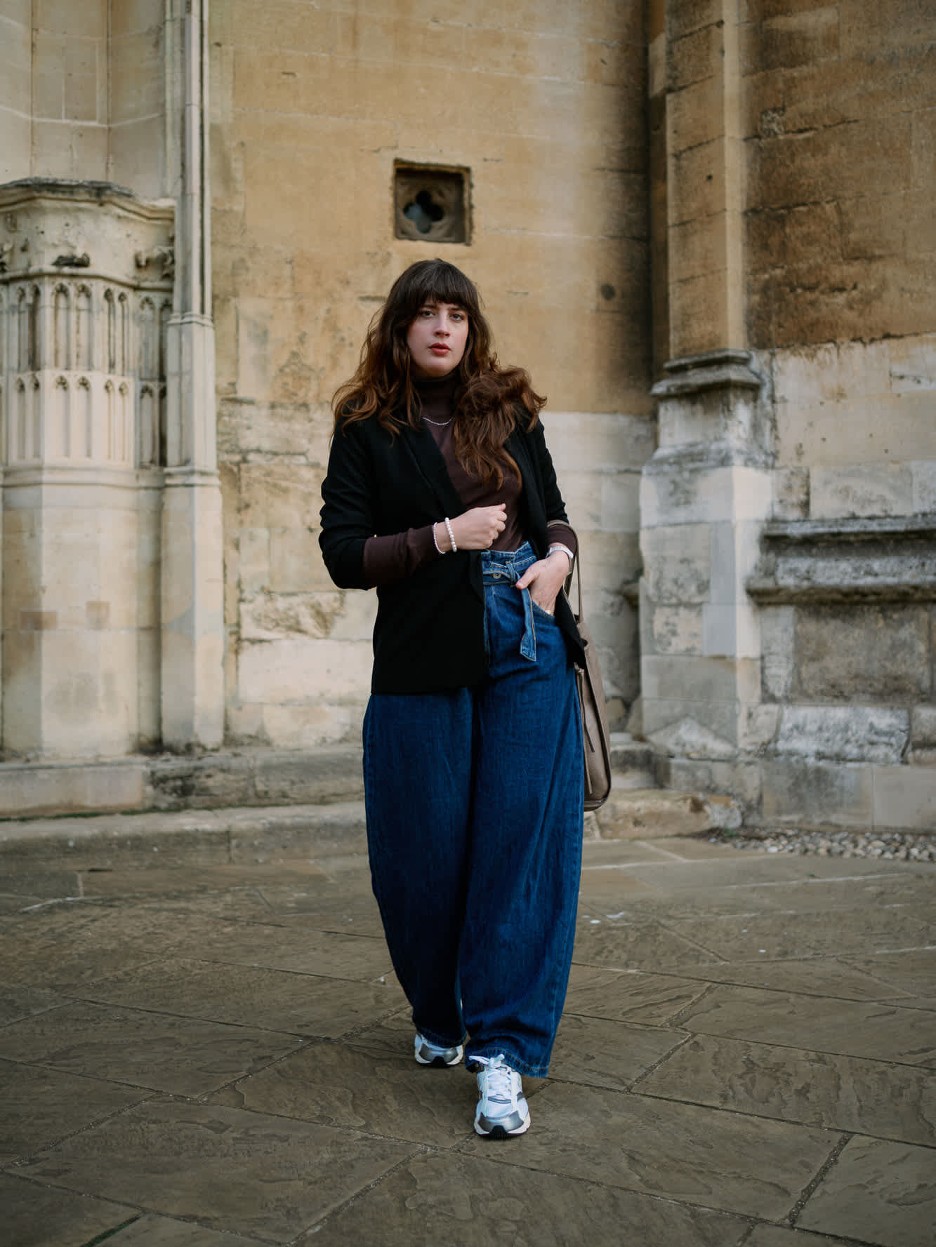 Frau mit schwarzem Blaze, blauer High-Waist-Jeanshose und weßen Sneakern