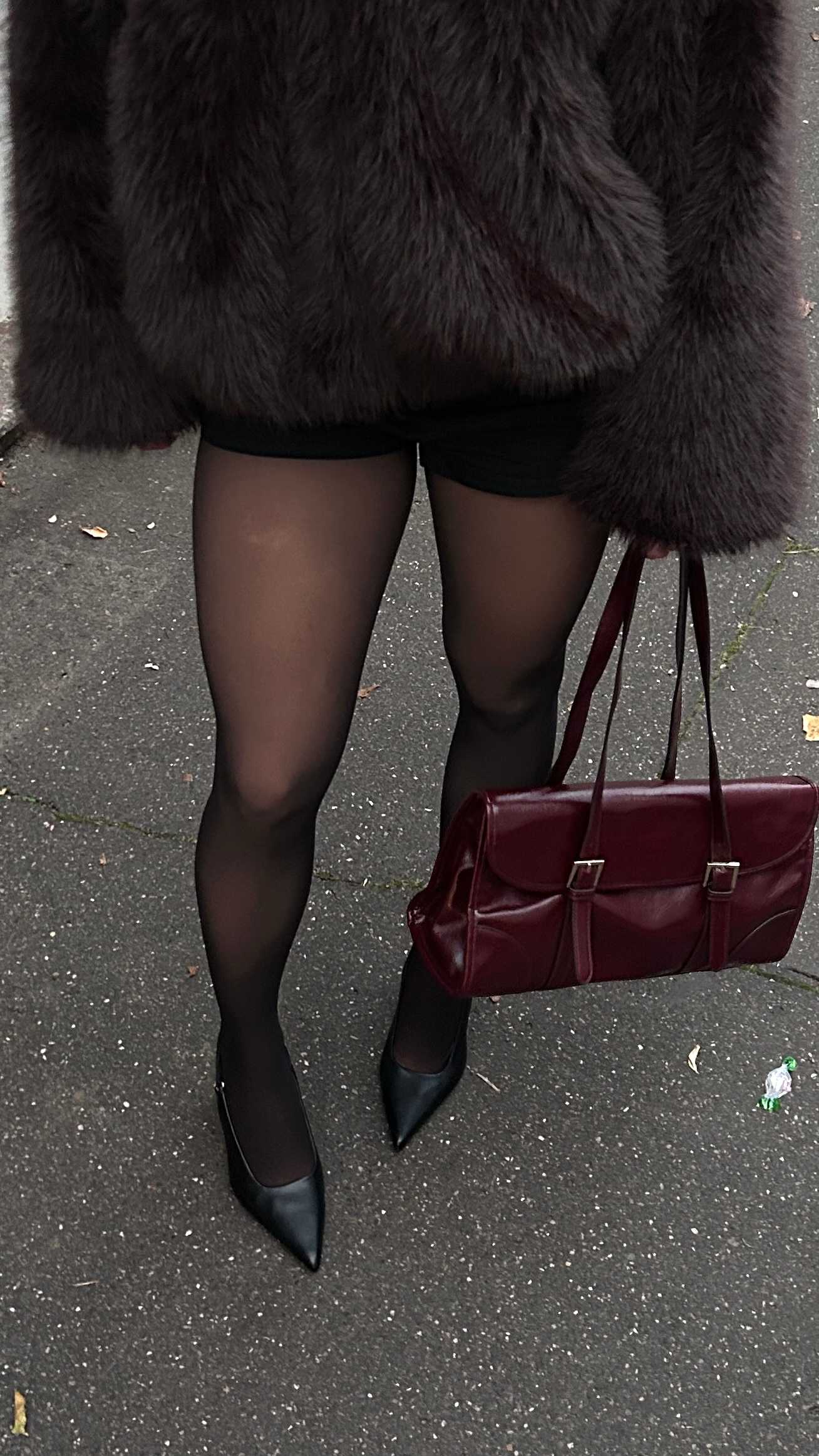 Frau trägt grauen Fellmantel, kombiniert mit Netzstrumpfhose und roter Handtasche