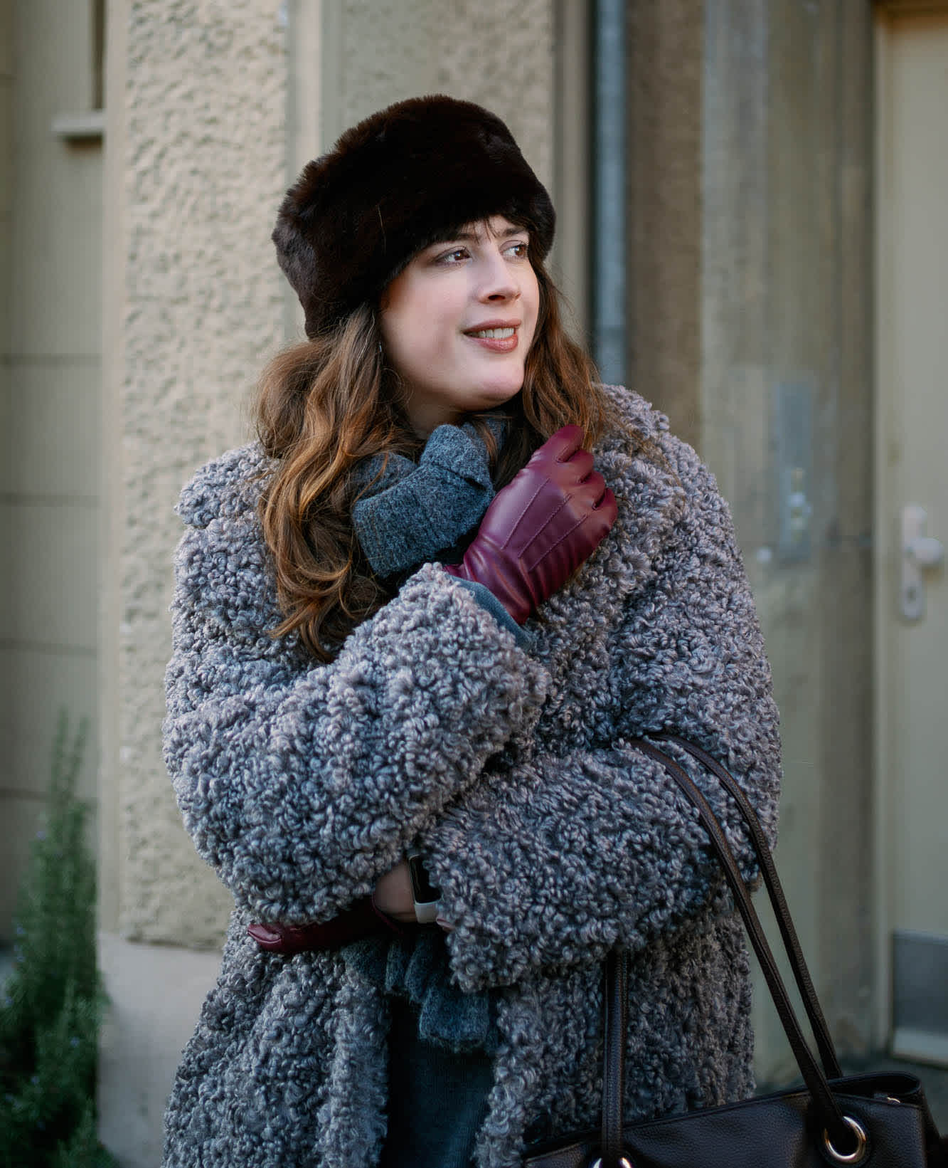 Junge Frau trägt grauen Flauschmantel, mit Handschuhen und Mütze