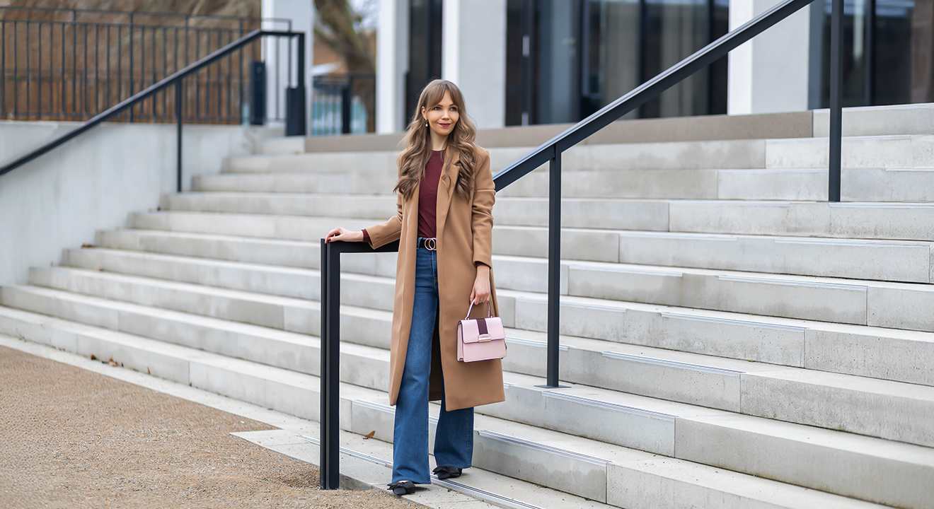 Frau in braunem Parka, trägt rosa Handtasche, steht an Treppengeländer