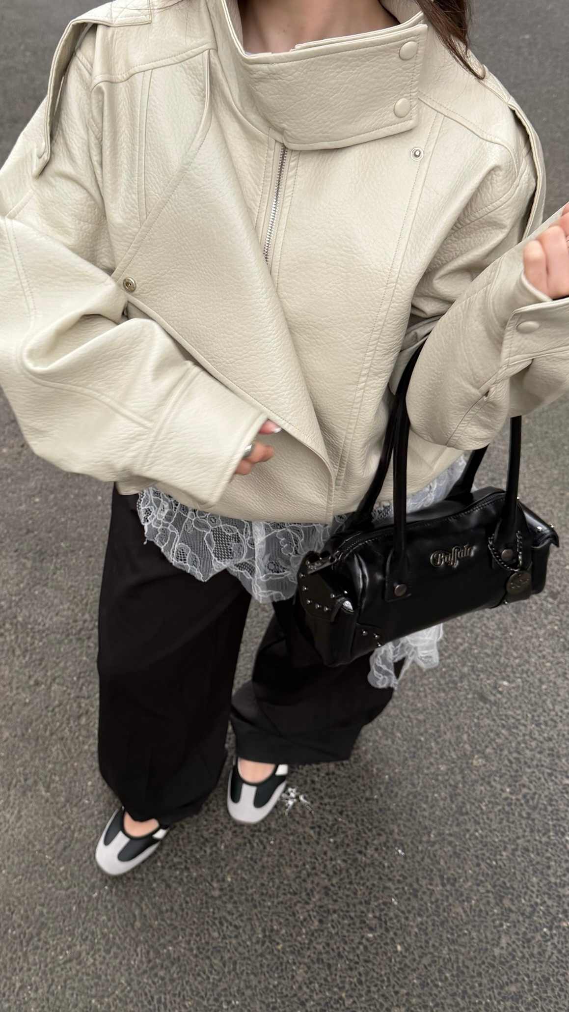 Creme-schwarzer Look. Fokus auf der hellbeigen Oversize-Jacke und dem darunterliegenden Mesh-Detail. Dazu sportliche Riemchen-Ballerinas und eine verzierte schwarze Handtasche.