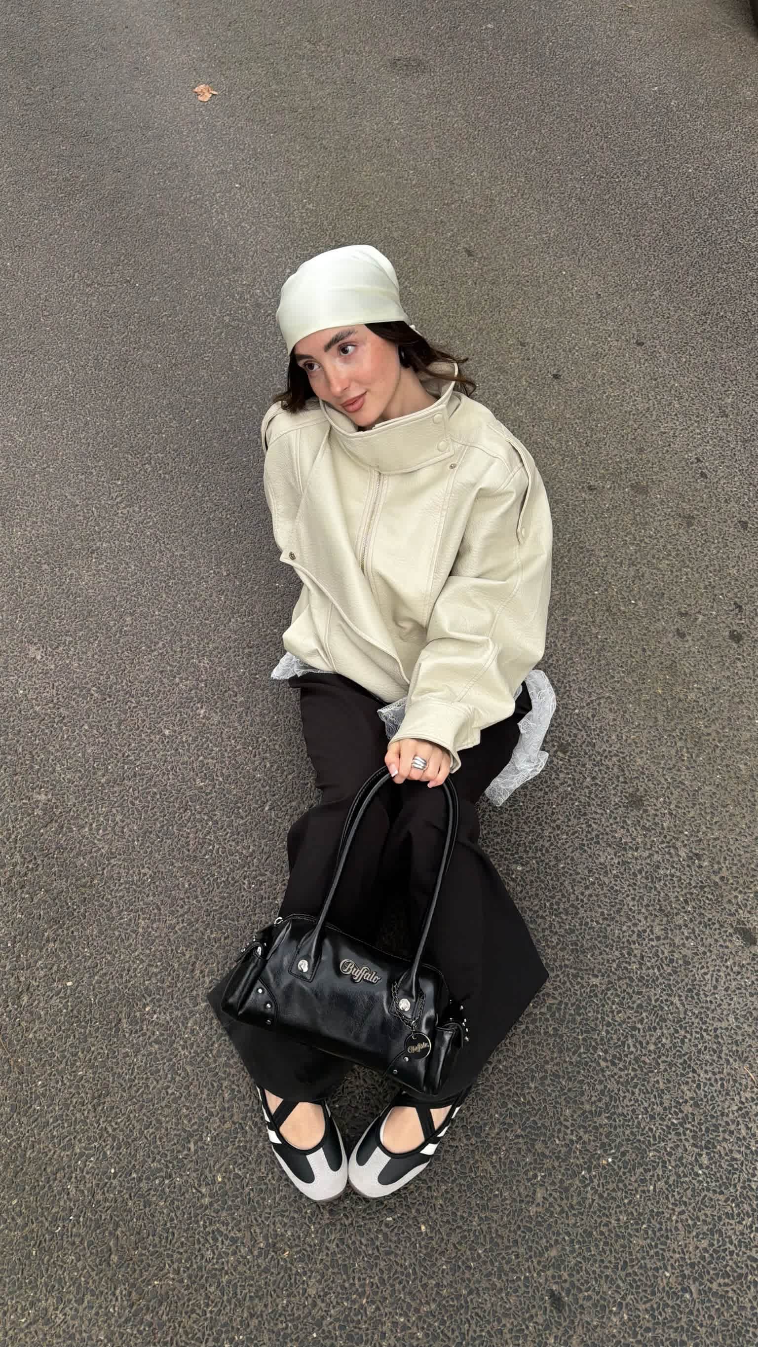 Frau präsentiert Creme-schwarzen Look mit Mesh-Detail. Im Fokus: Sportliche Riemchen-Ballerinas und verzierte schwarze Handtasche.