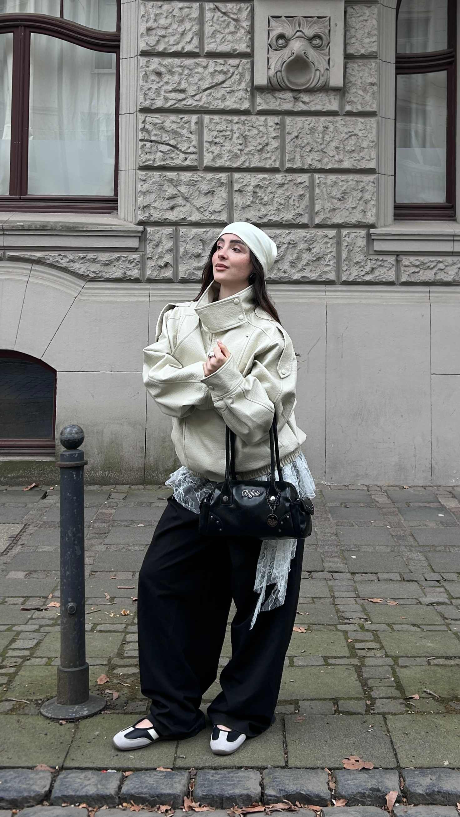 Schwarz-weiße Riemchen-Ballerinas im Sneaker-Look. Urbaner Style mit cremefarbener Lederjacke, weißem Mesh-Element, schwarzer Tasche und weiter schwarzer Hose.