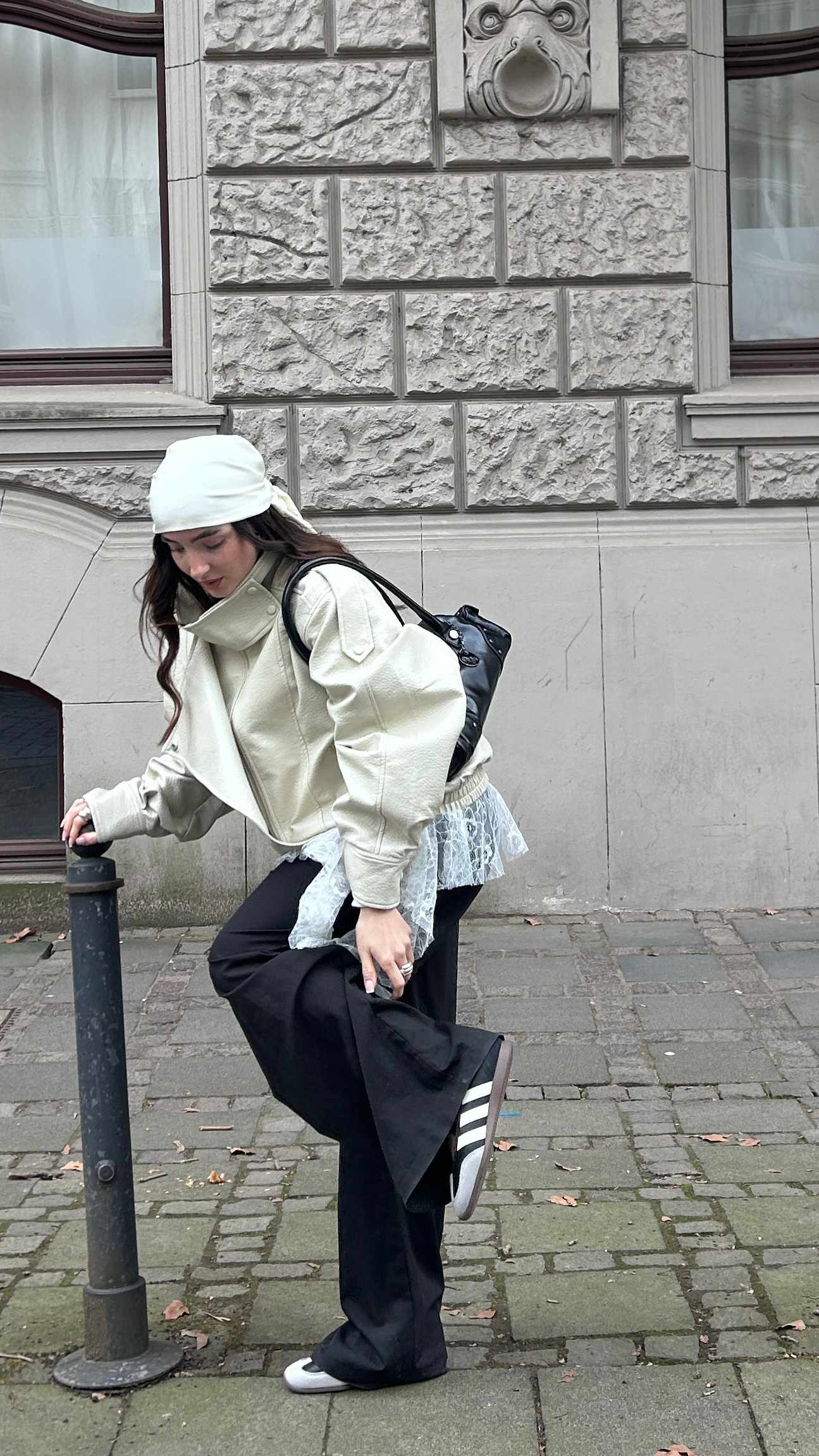 Blick auf Kontrast zwischen cremefarbener Oversize-Jacke und weißem Spitzen-Mesh. Dazu weite schwarze Hose und sportliche Sneaker im klassischen Streifen-Design.