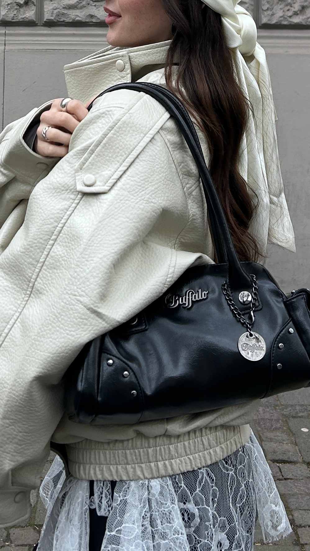 Fokus auf der cremefarbenen Oversize-Lederjacke und dem markanten Spitzen-Mesh-Detail. Dazu kombiniert eine schwarze Buffalo-Tasche mit silbernen Nieten-Applikationen.