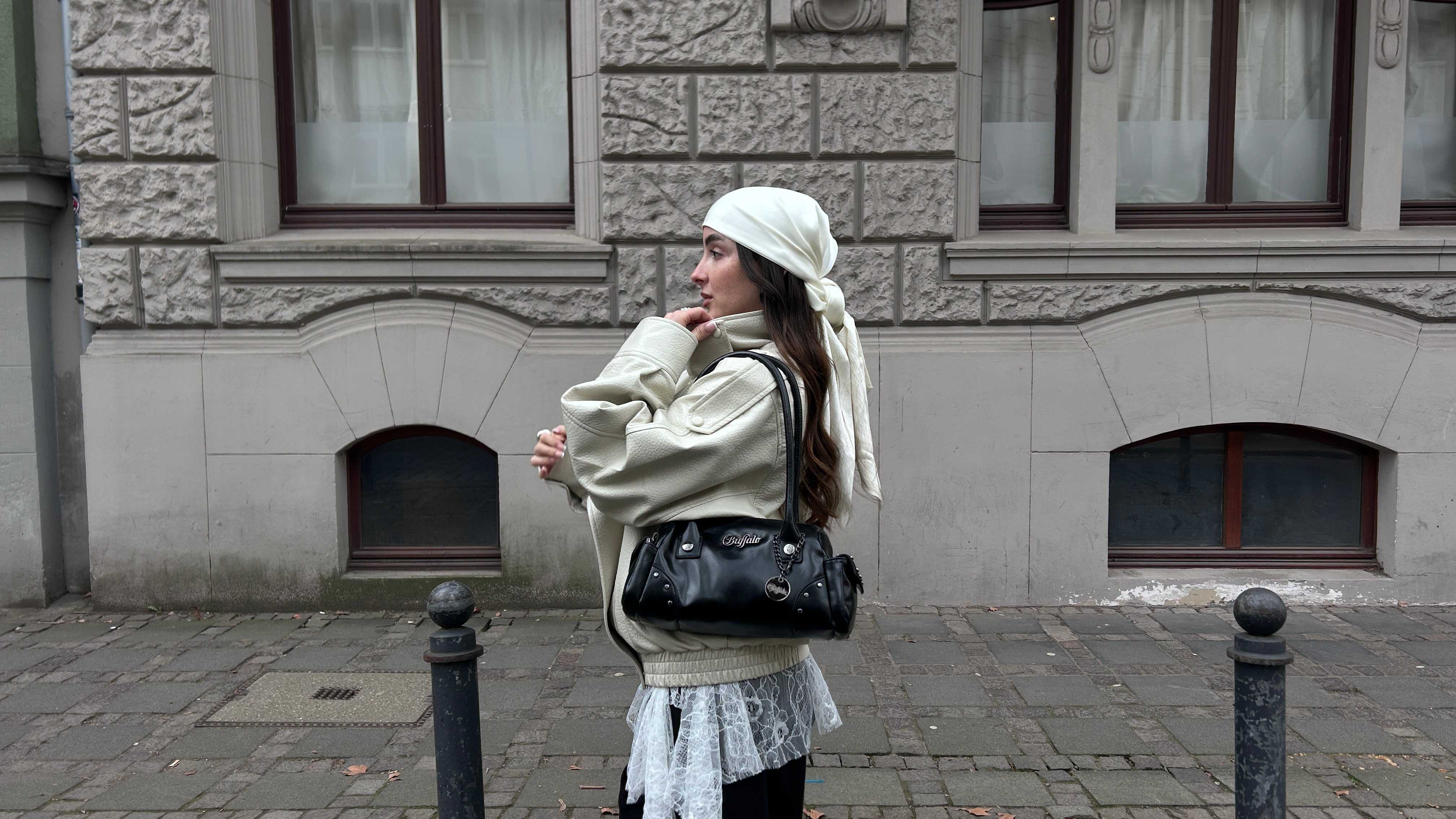 Cremefarbenes Kopftuch und passende Oversize-Lederjacke. Look mit weißem Mesh-Detail und schwarzer Buffalo-Tasche.