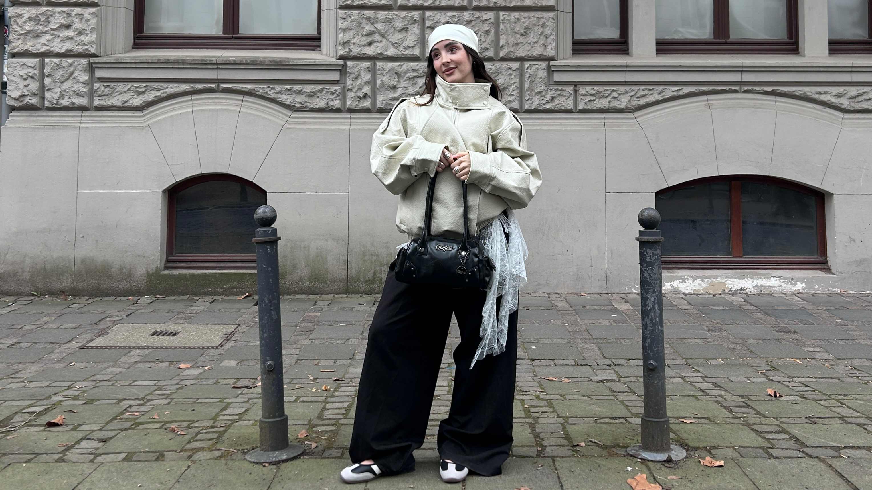 Outfit schafft prägnante Silhouette durch Oversize-Jacke, Mesh-Lagenlook und weite Hose. Abgerundet durch sportliche Riemchen-Ballerinas und eine schwarze Handtasche.