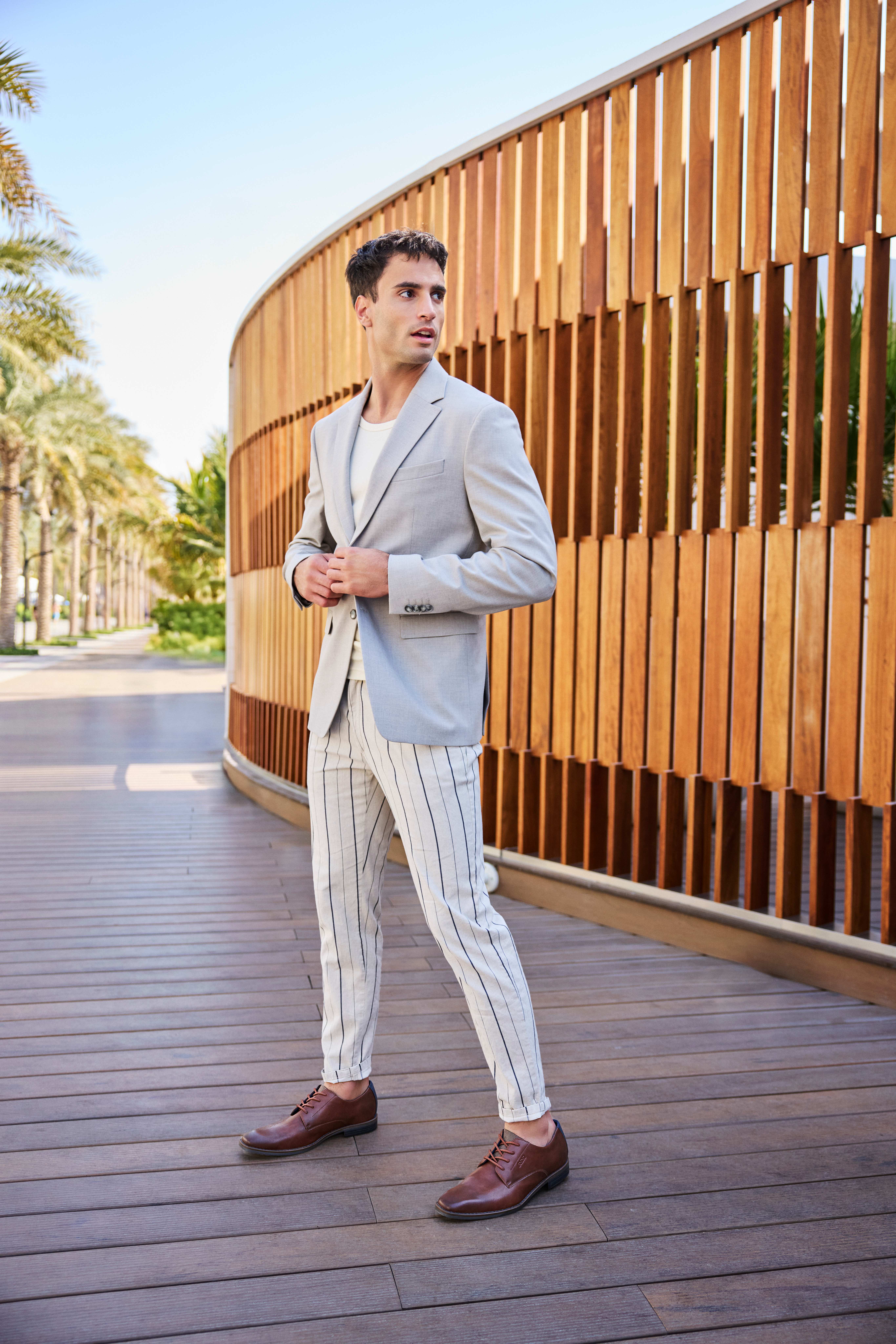 Mann in grauem Business Casual-Look, posiert auf Strandpromenade
