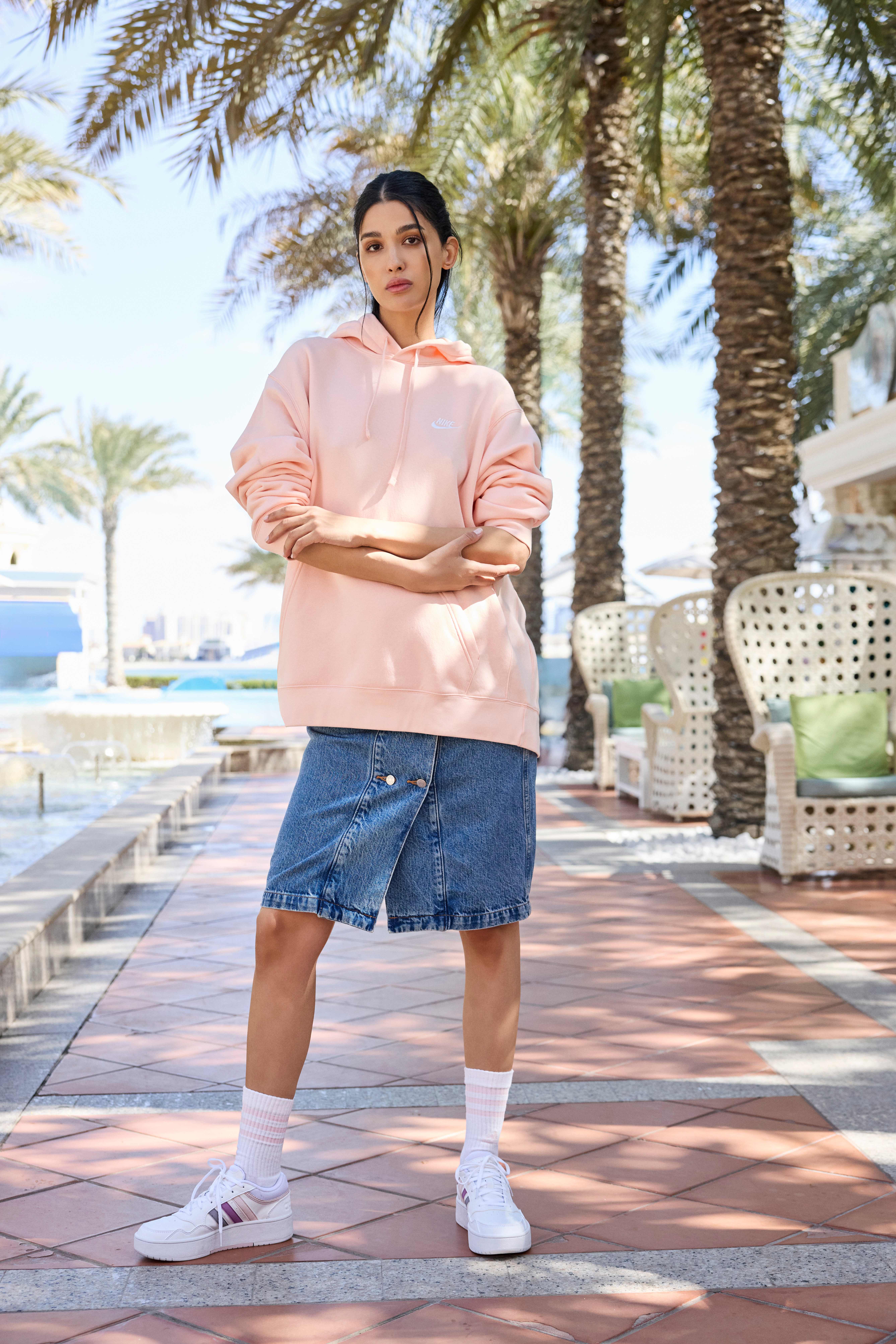 Frau mit sportlichem Oversize-Sweater, kombiniert mit Denim Rock, weißen Socken und passenden Sneakern