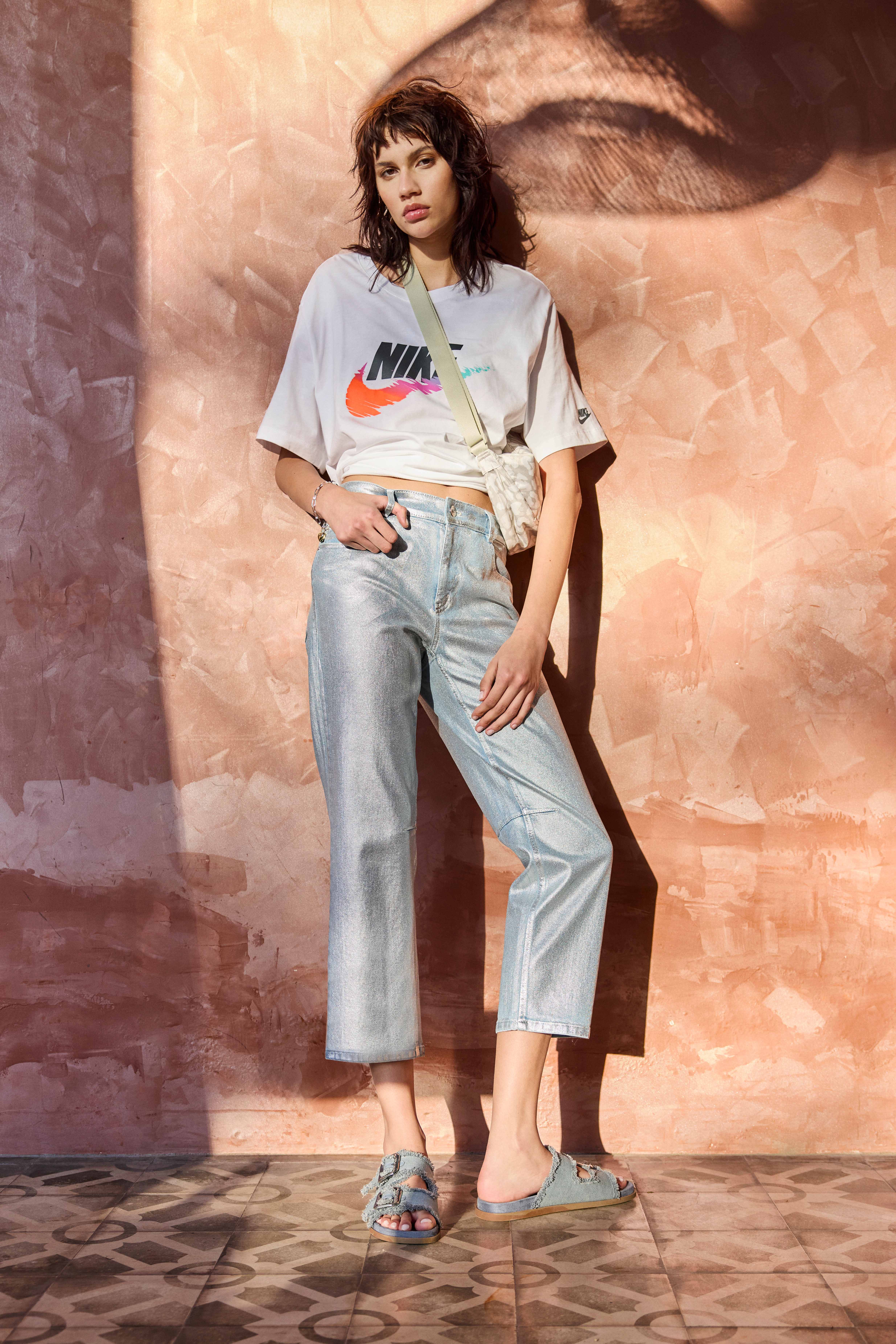 Frau in lässigem Outfit mit Nike-Shirt, langer Jeanshose und farblich passenden Sandalen