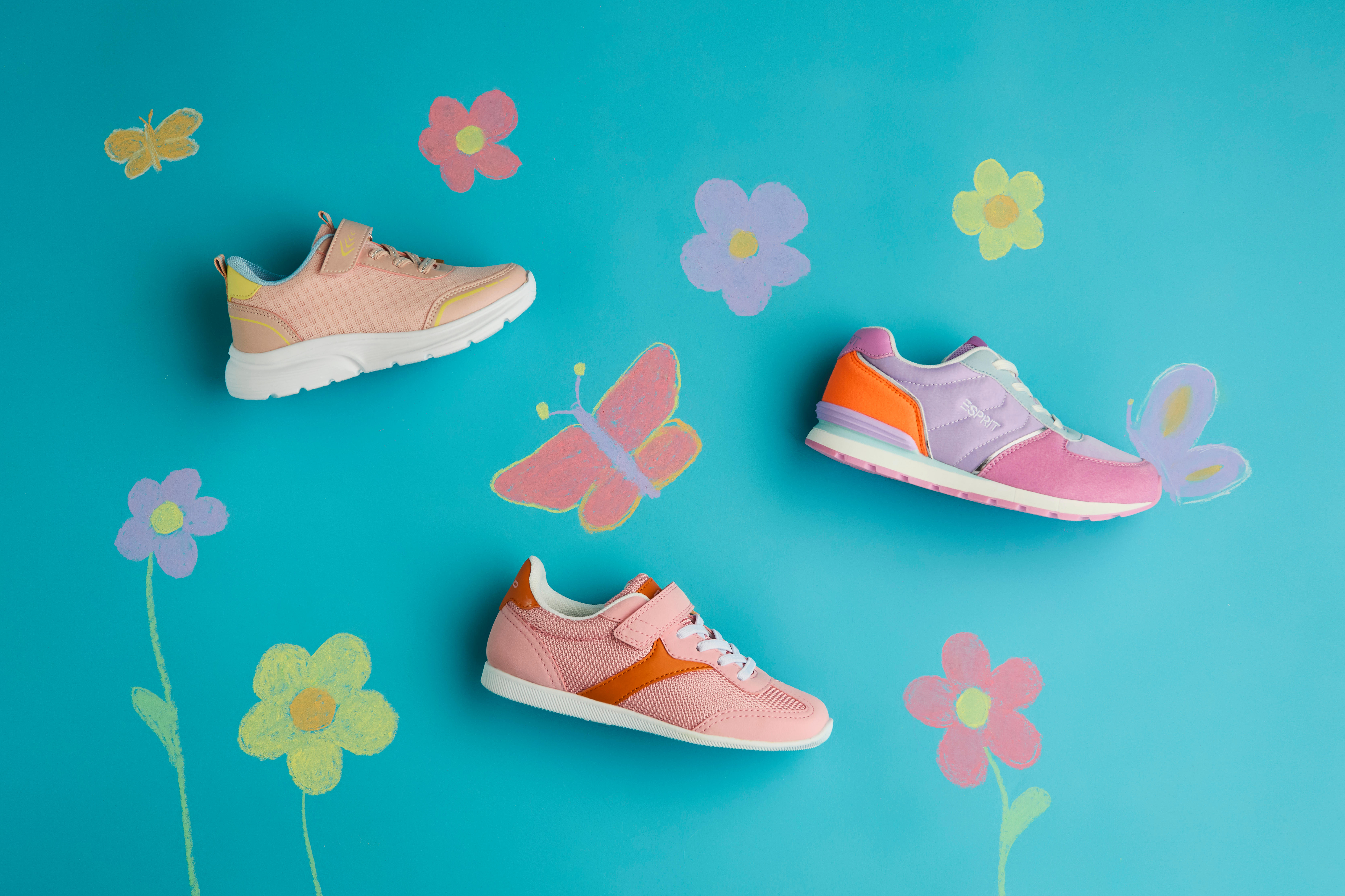 Rosa und beigefarbene Kinderschuhe neben gemalten Blümchen und Schmetterlingen