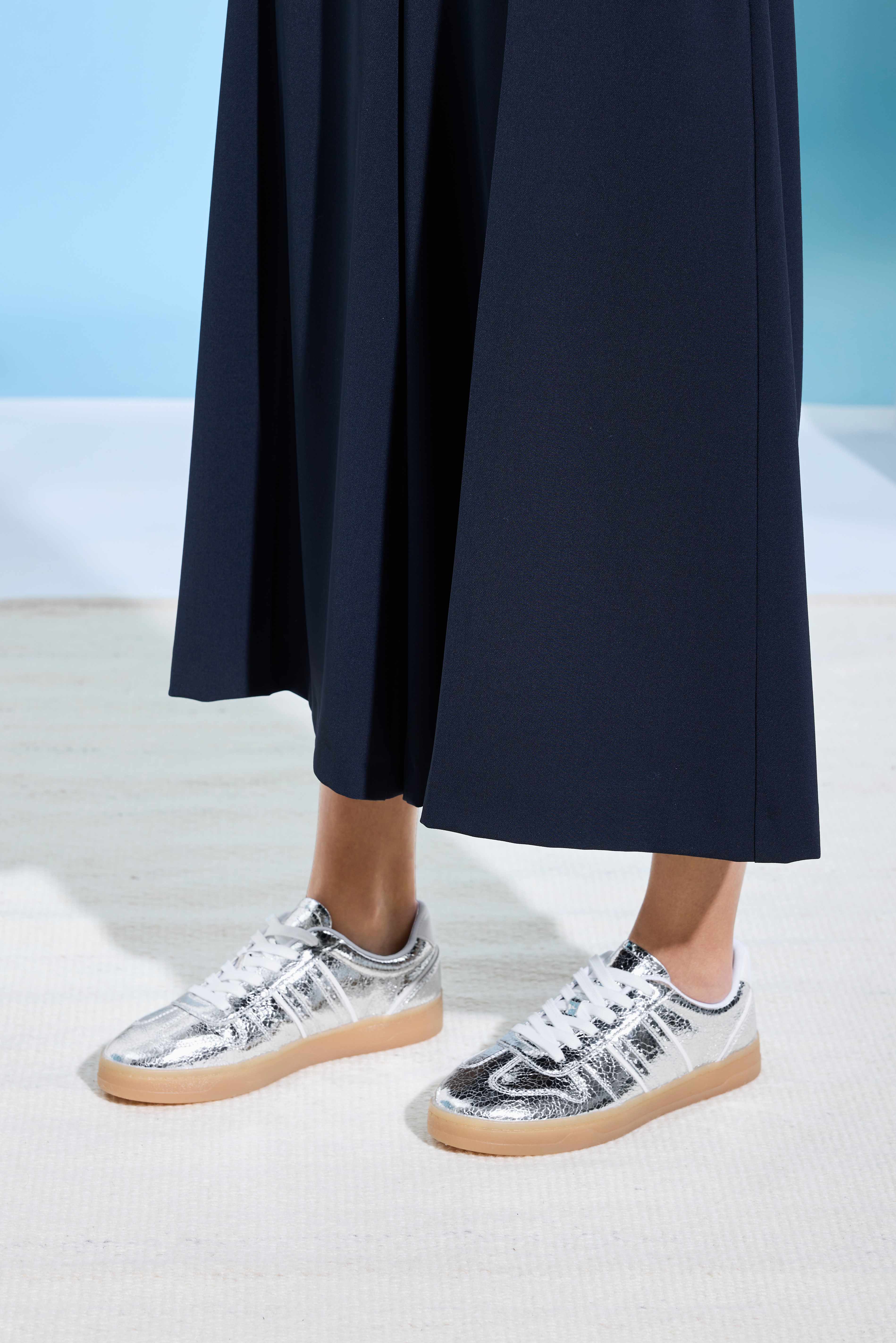 Frau in tiefblauem, langen Rock trägt flache Sneaker in Weiß