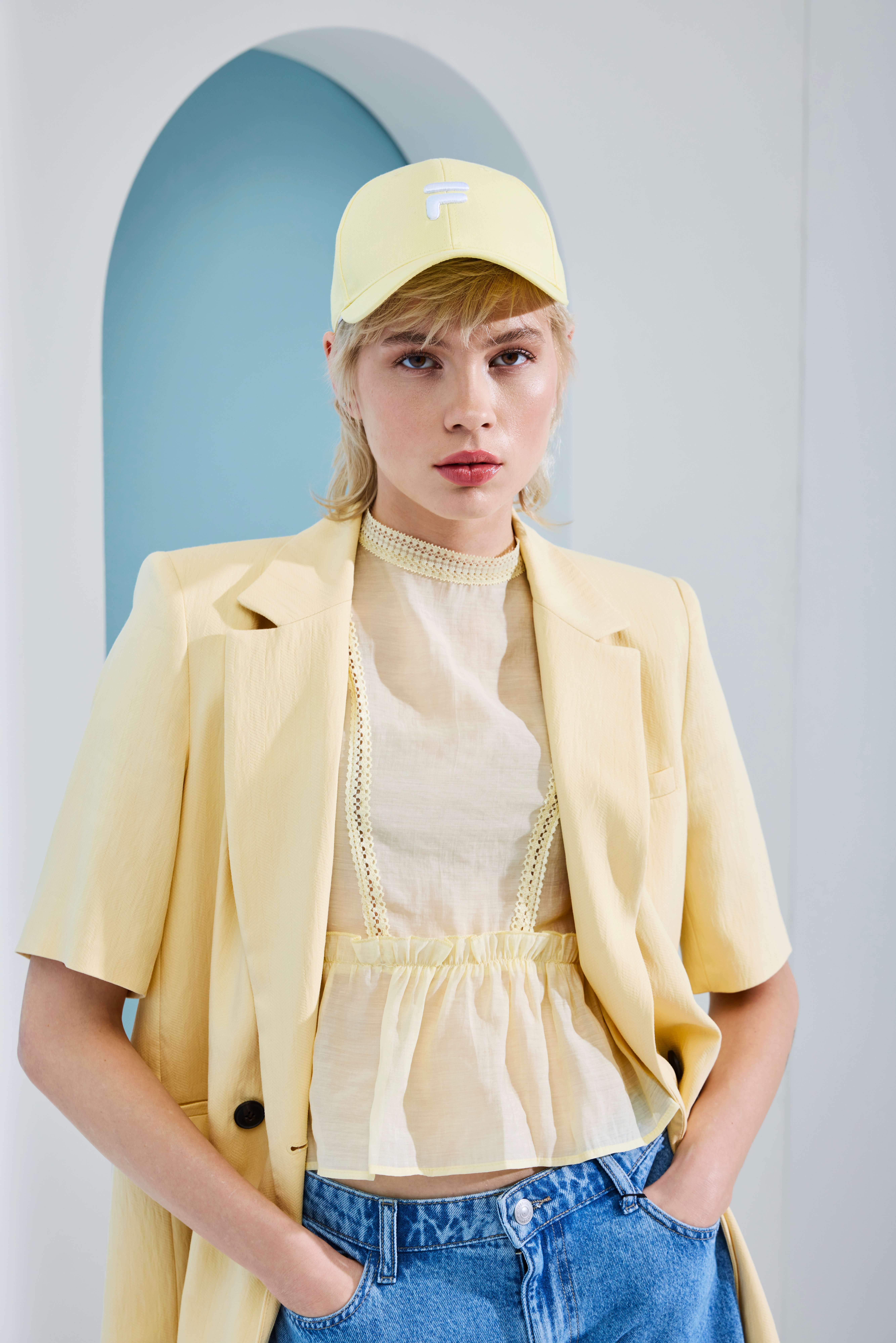 Frau trägt buttergelben Blazer in Kombination mit transparentem Top und Denim-Shorts