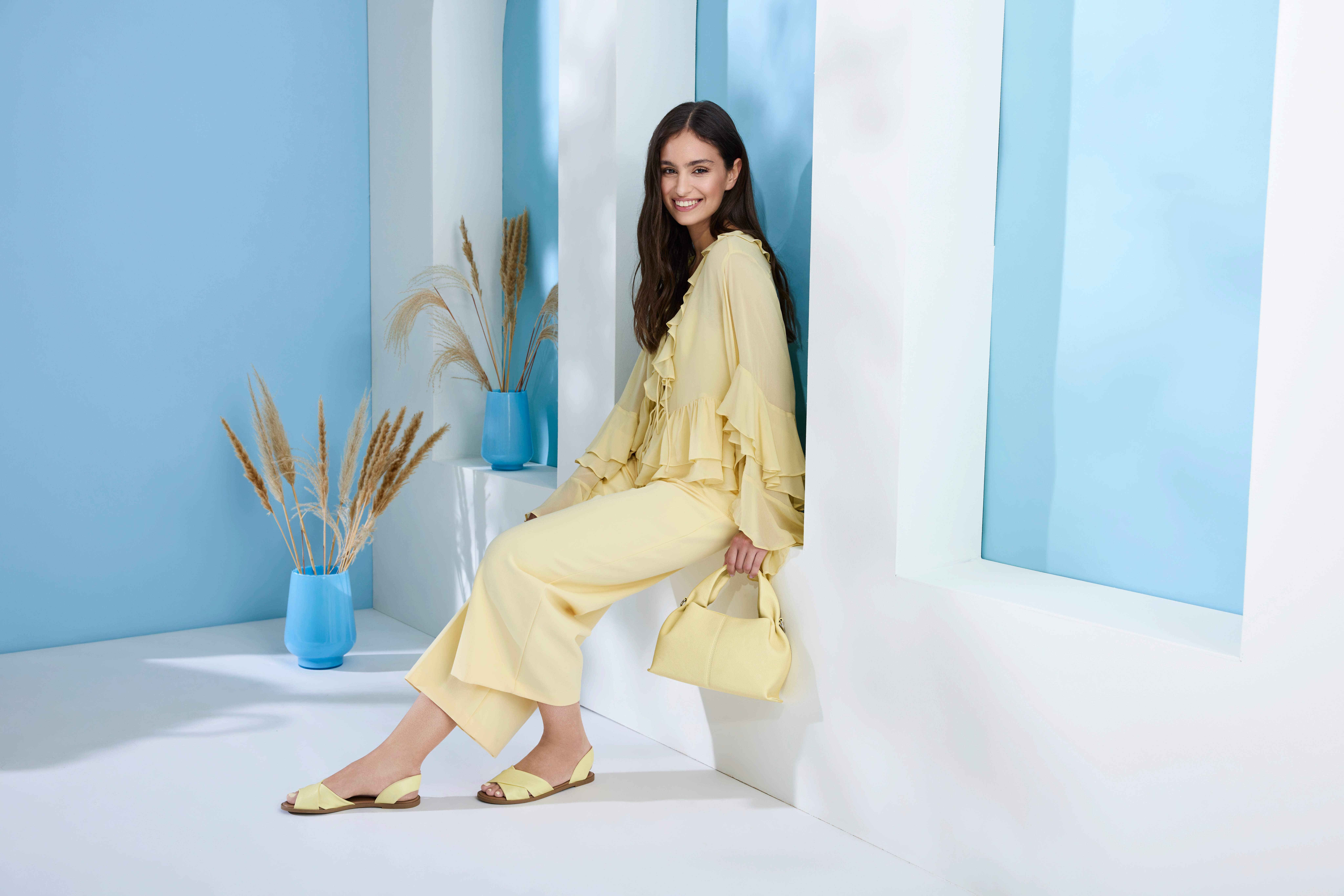 Schwarzhaarige Frau sitzt in weißem Torbogen, trägt Outfit in Butter Yellow-Farbton