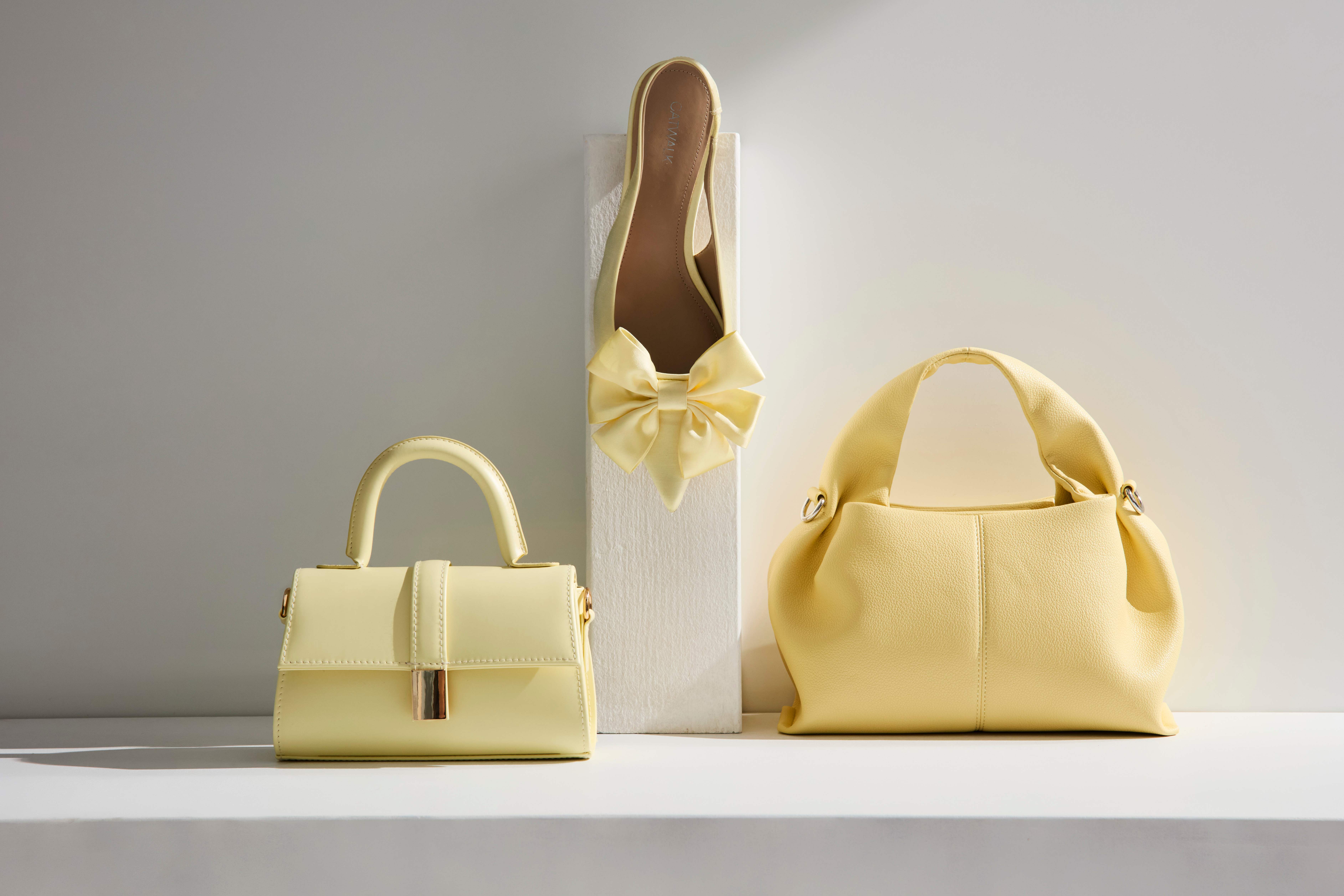 Zwei gelbe Handtaschen neben gelbem Pumps mit Schleife