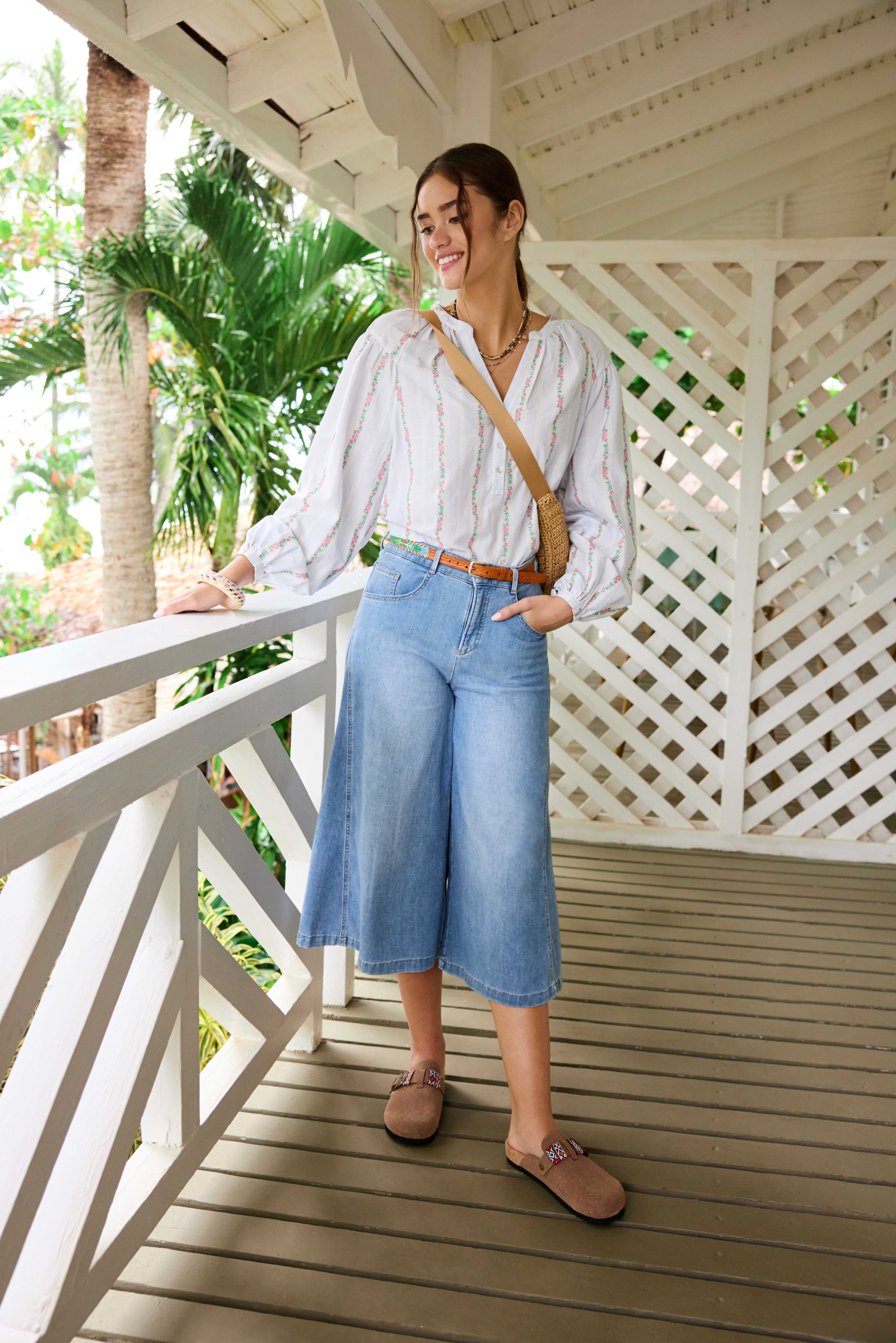 Blonde Frau in weißem Boho-Style-Top und Wide Leg Denim-Pants, steht auf Veranda