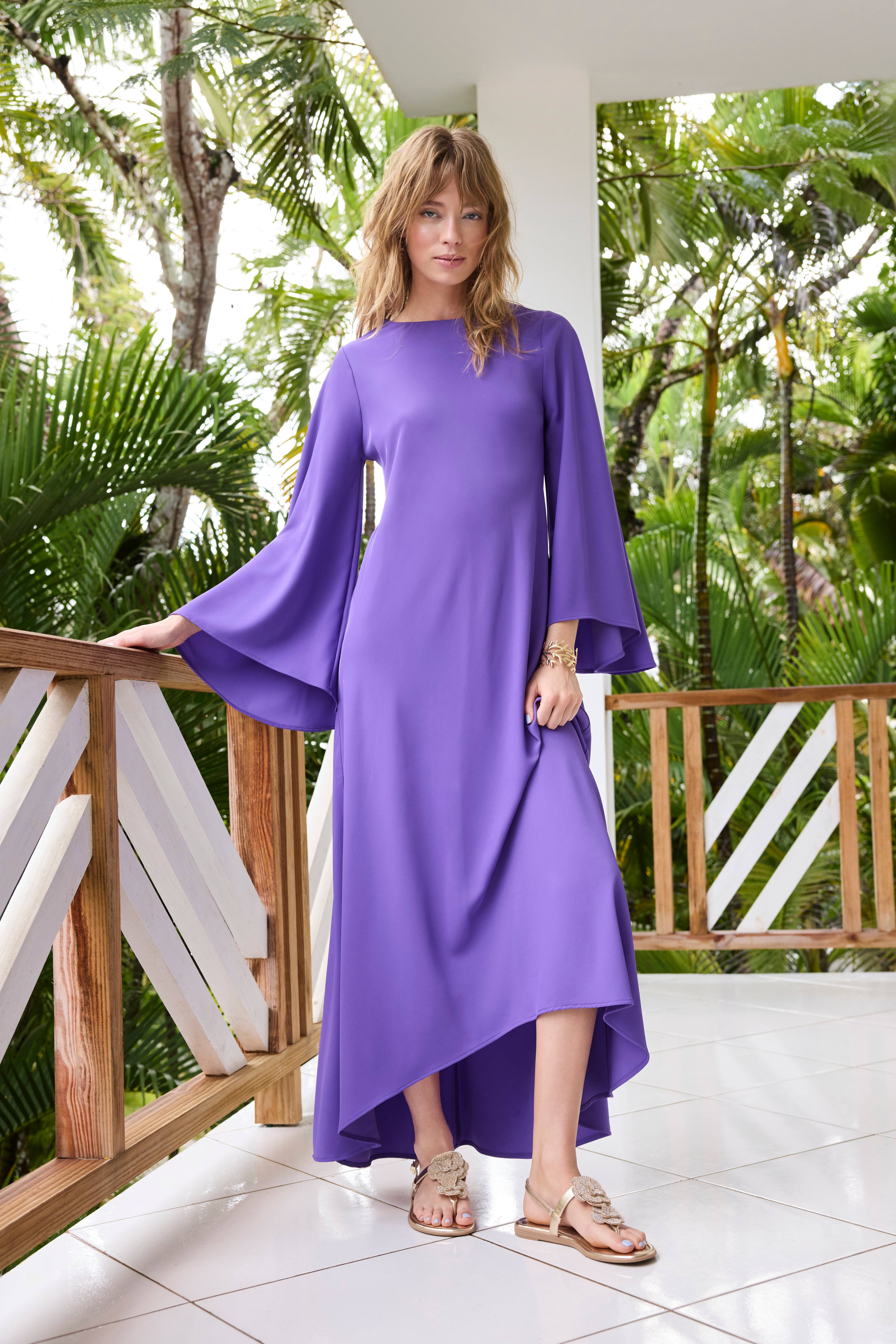 Frau in lila Maxikleid, trägt Sandaletten mit Blumen, lehnt an Geländer einer Veranda