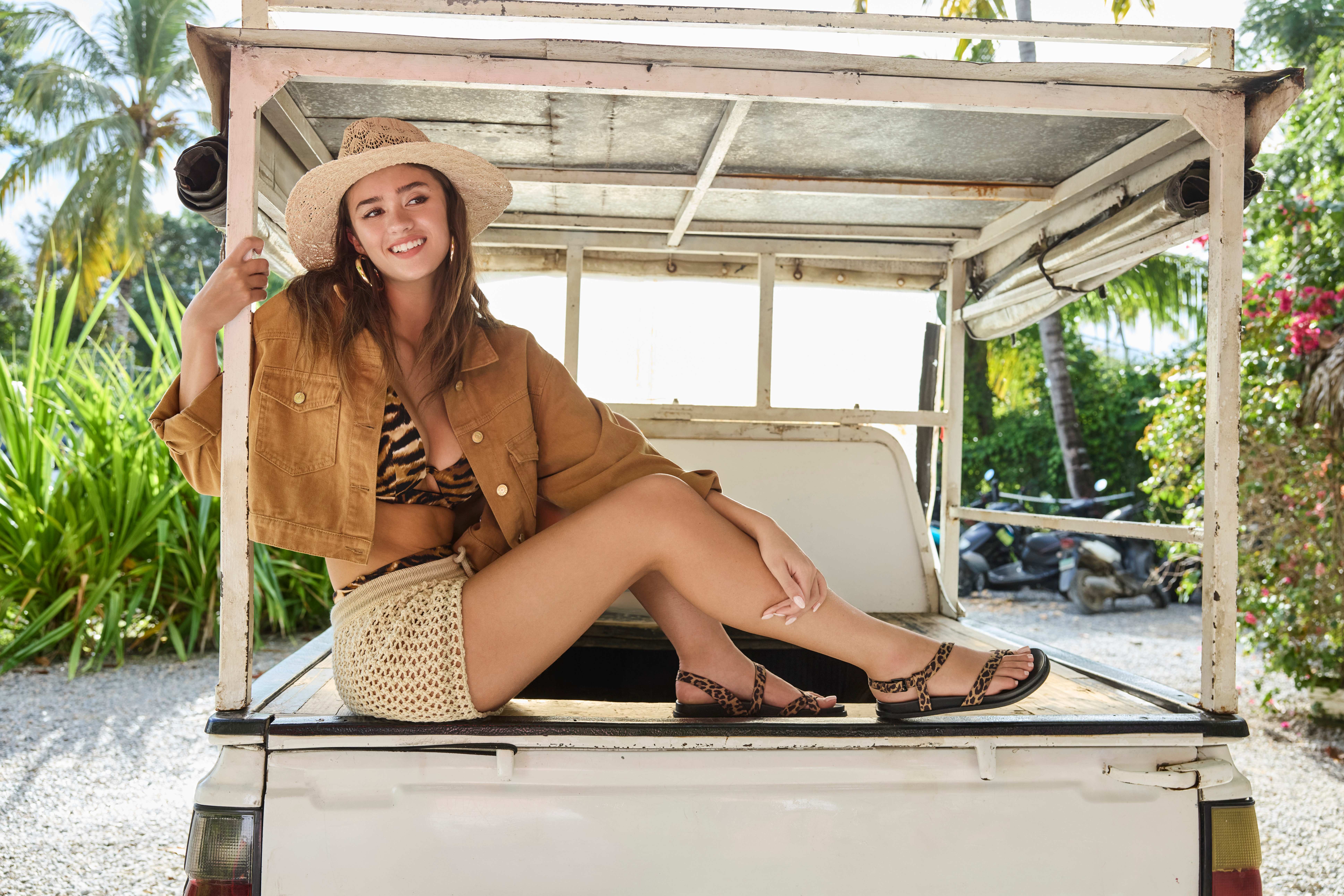 Frau in sandfarbenem Top, trägt Animalprint-BH und passende Shorts, sitzend auf Ladefläche eines Trucks