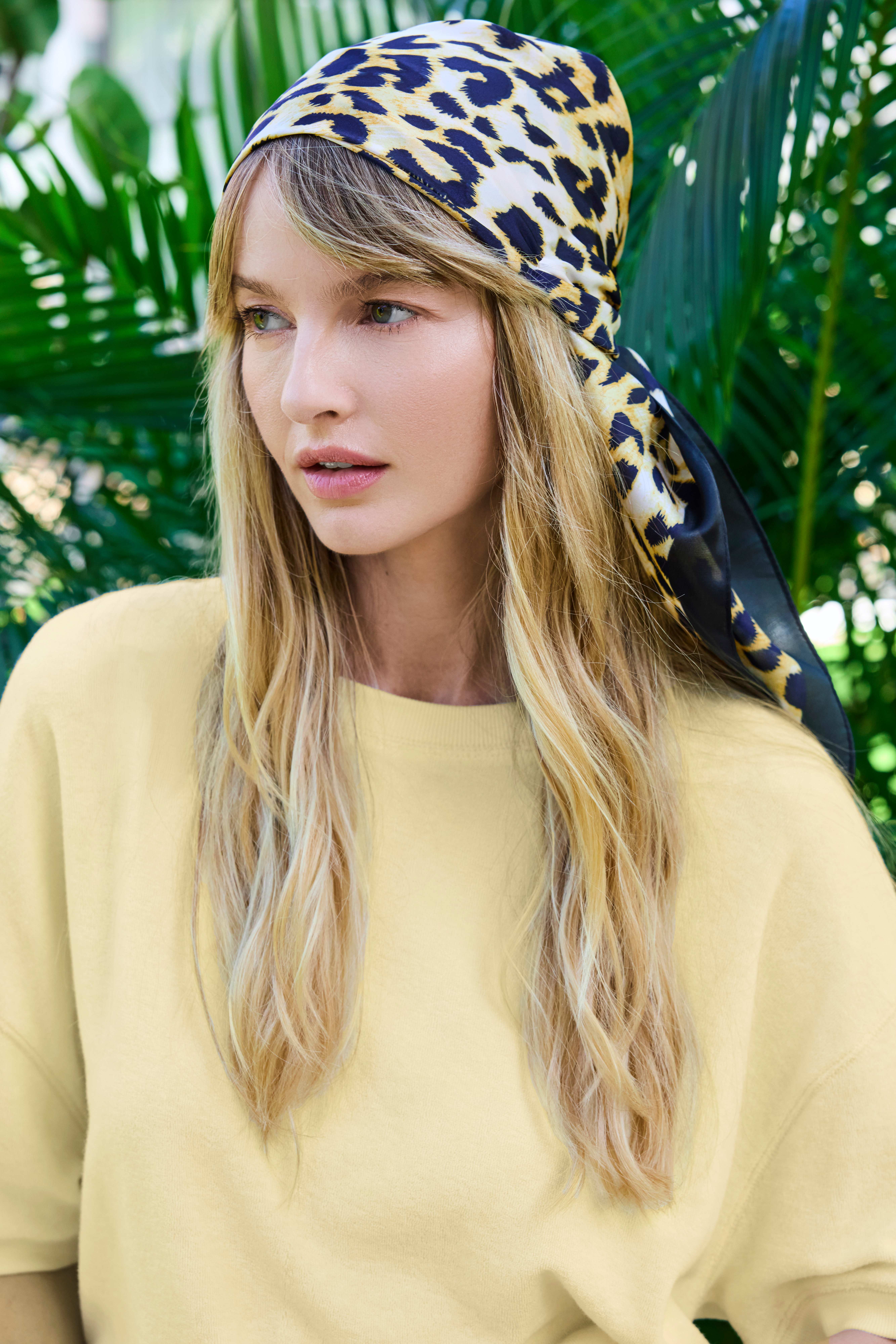 Frau vor Dschungel-Kulisse, trägt Animalprint-Kopftuch zu hellgrauem Pullover