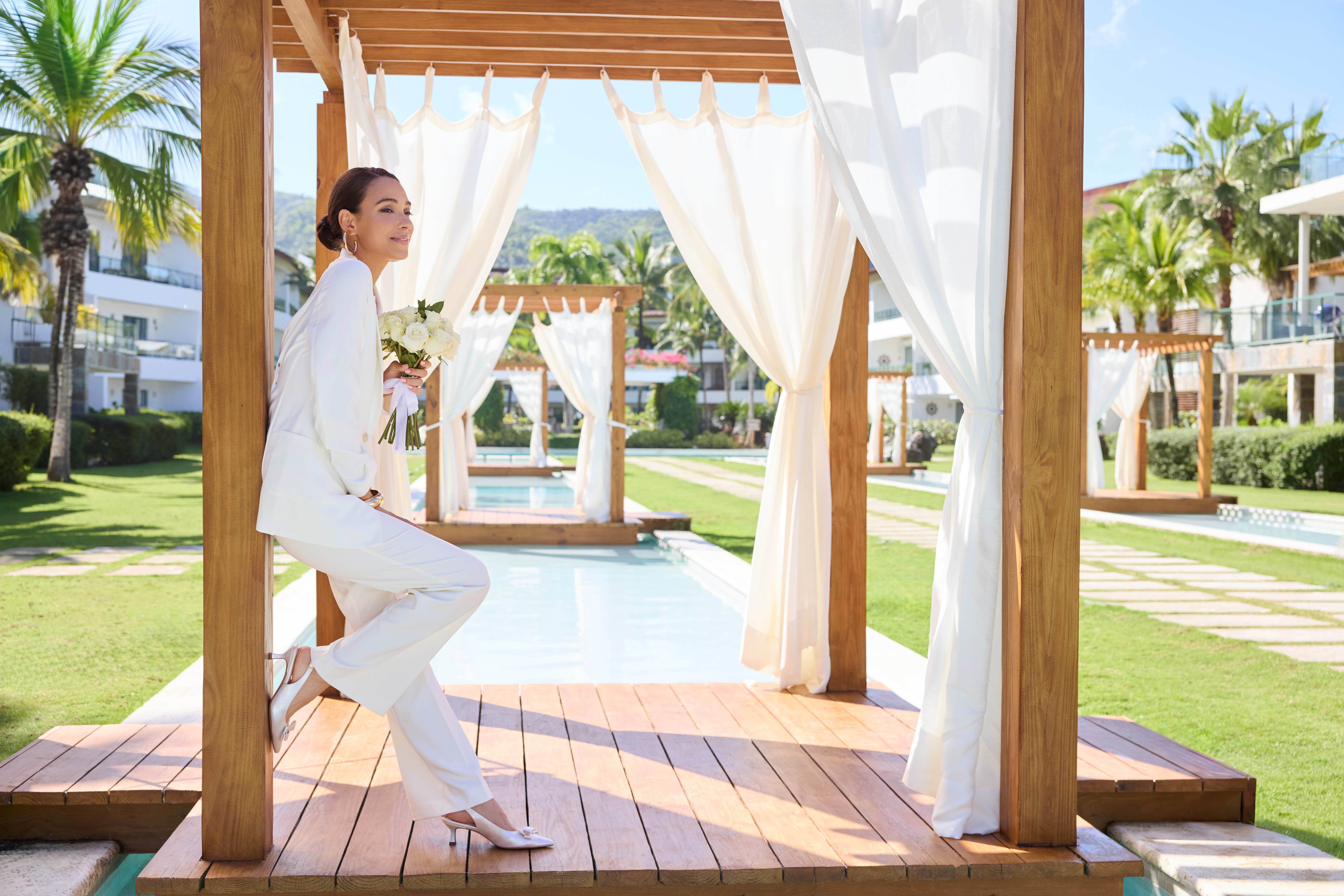 Frau in reinweißem Outfit steht in Holz-Pavillon vor Spa-Kulisse