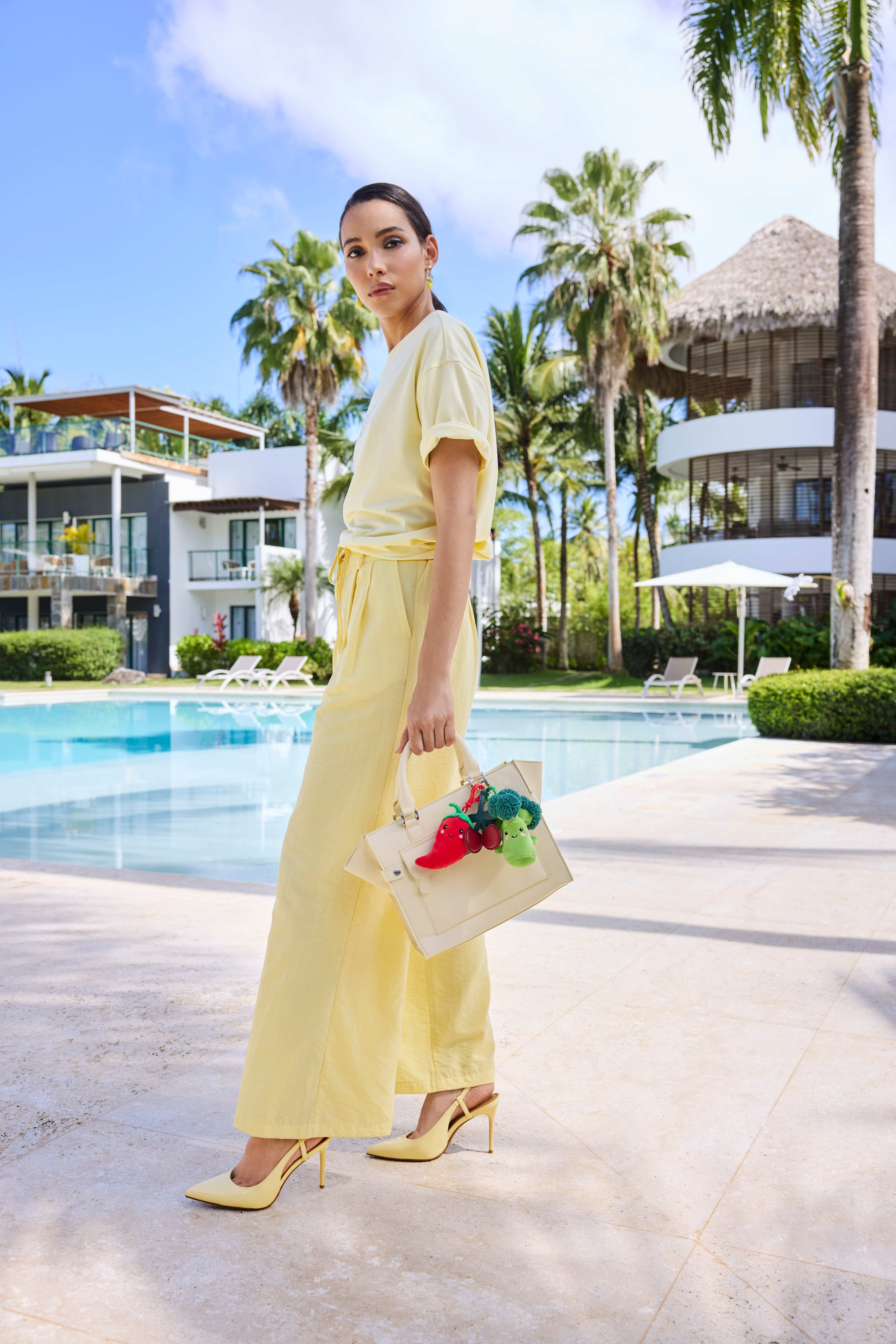 Frau in hellgelbem Sommerkleid und Heels steht neben Pool