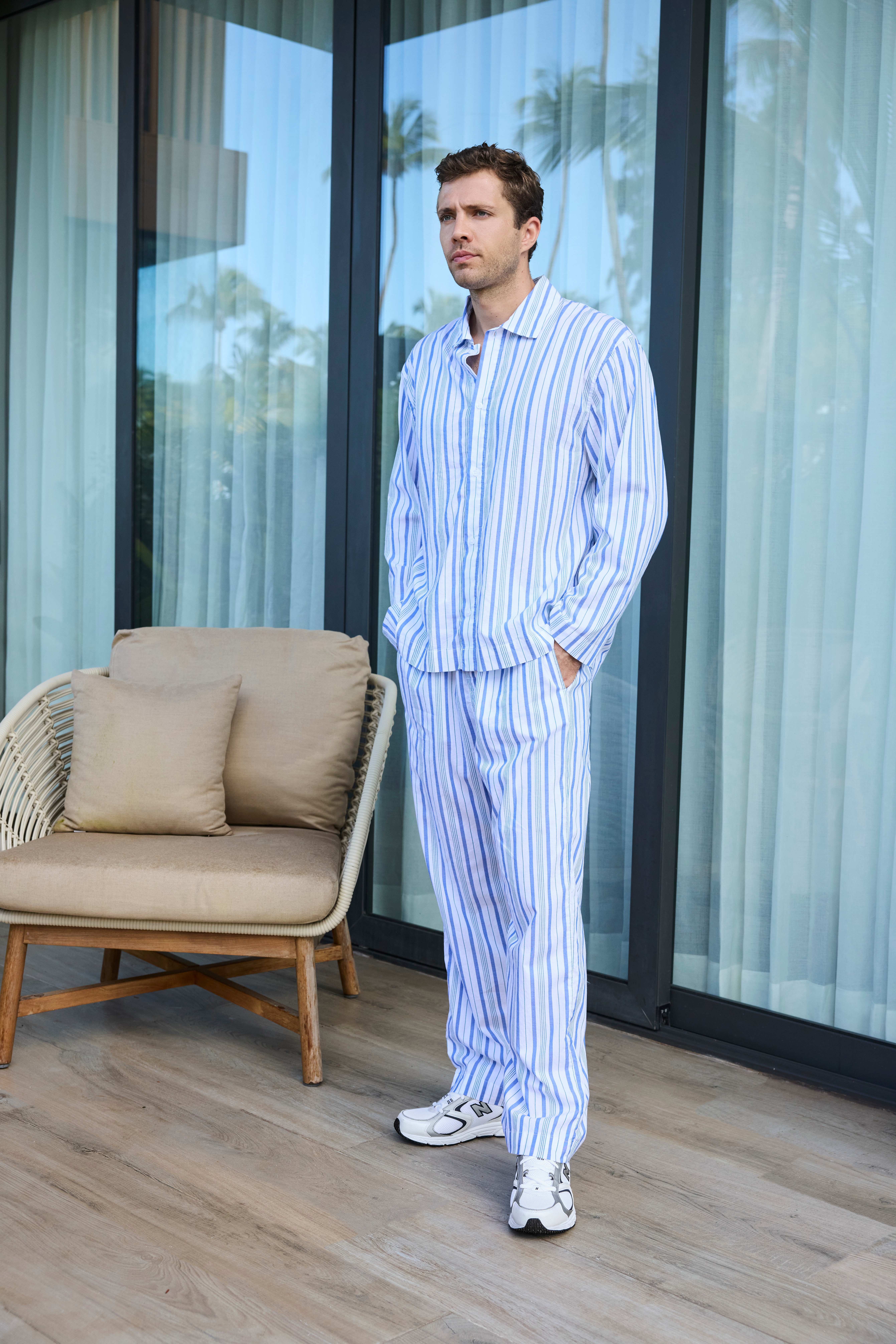 Mann in blau-weiß gestreiftem Pyjama, stehend in Sneakern auf Terrasse