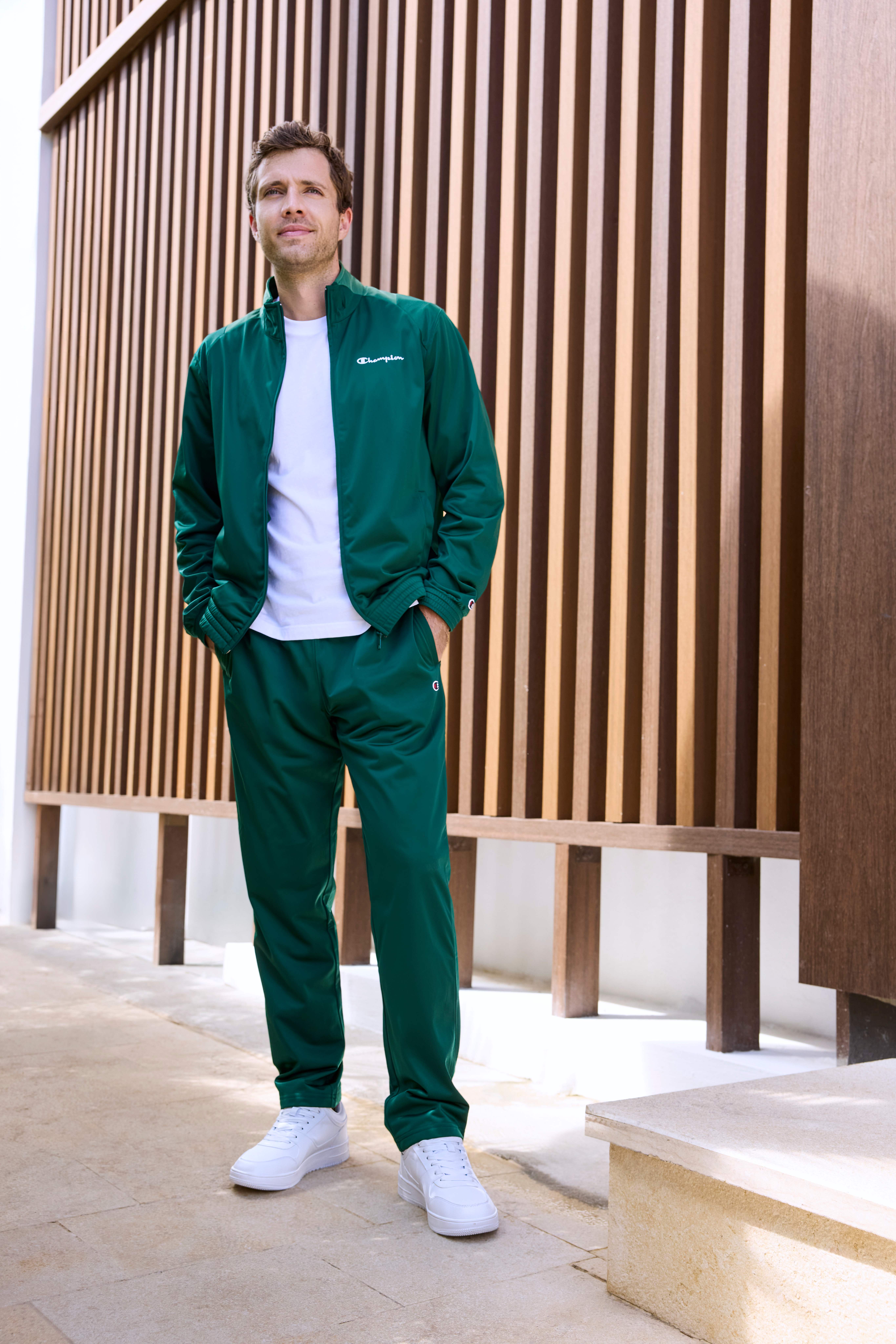 Mann steht lässig in grünem Jogginganzug, kombiniert mit weißem Shirt