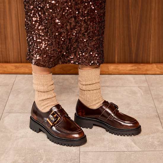 Frau mit bronzenem Strasskleid trägt hellbraune Socken zu Dandy-Schuhen