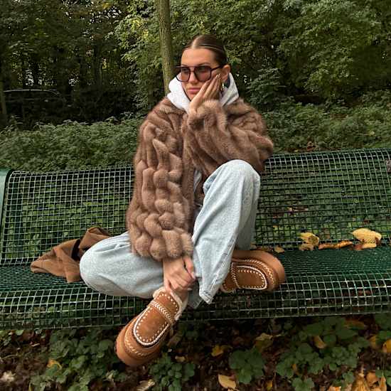 Frau sitzt auf Parkbank, trägt braunen Sweater und flauschige Slipper