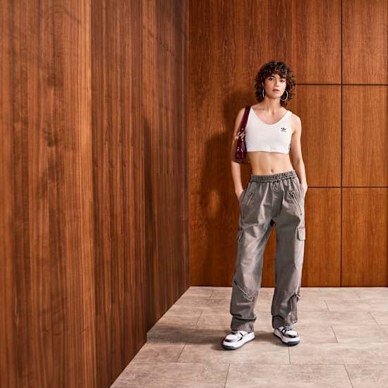 Frau in lässiger Low-Waist-Jeans mit weißem TankTop, stehend vor Holzwand