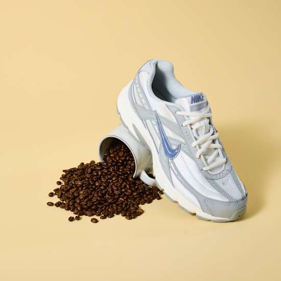 Weißer Nike-Sneaker steht auf Tasse mit Kaffeebohnen