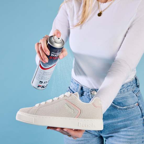 Frau in weißem Top ist dabei, Schuhe mit Imprägnierspray zu imprägnieren