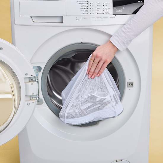 Person legt Schuhe in Wäschesack in eine Waschmaschine